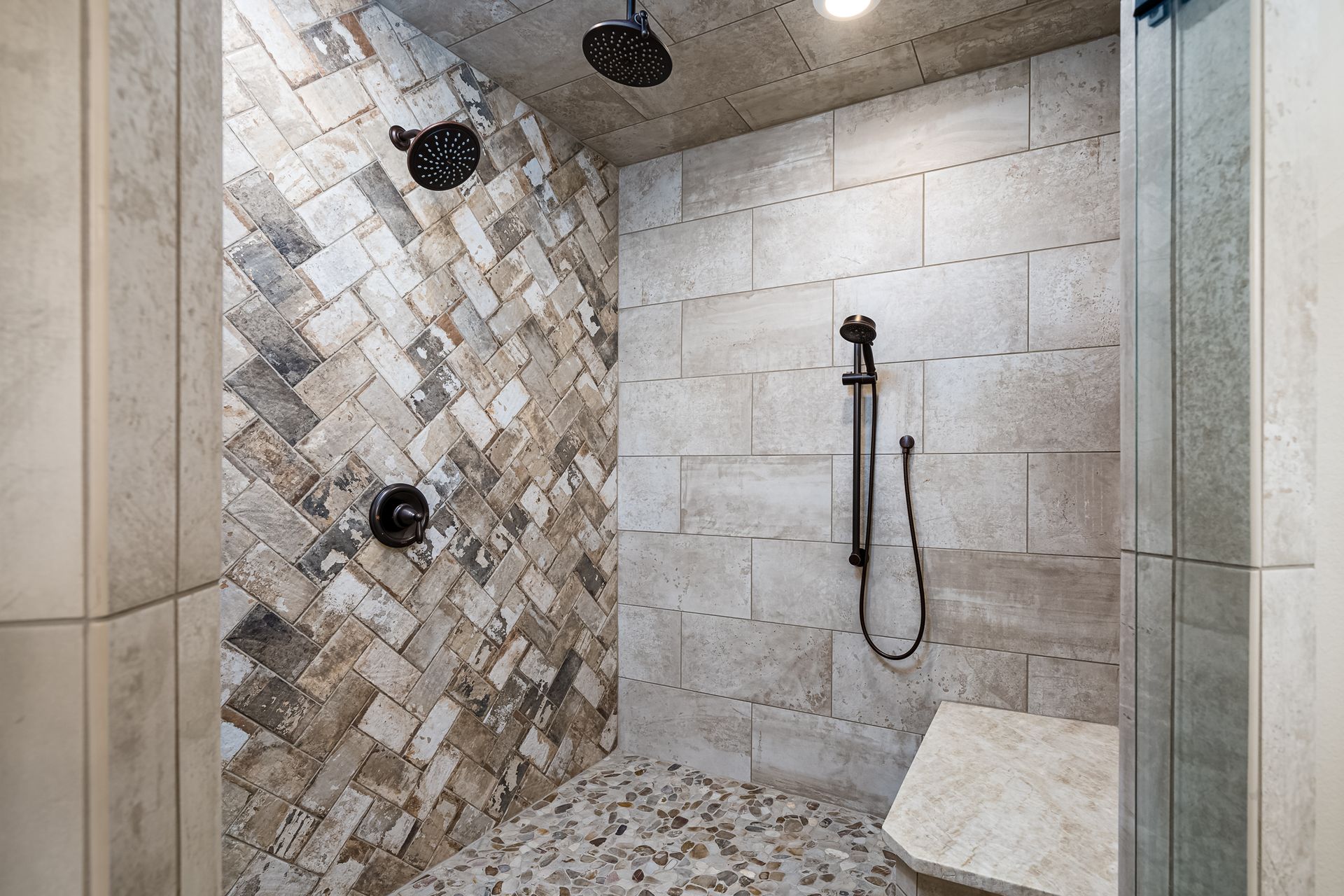 A walk in shower with two shower heads and a bench.