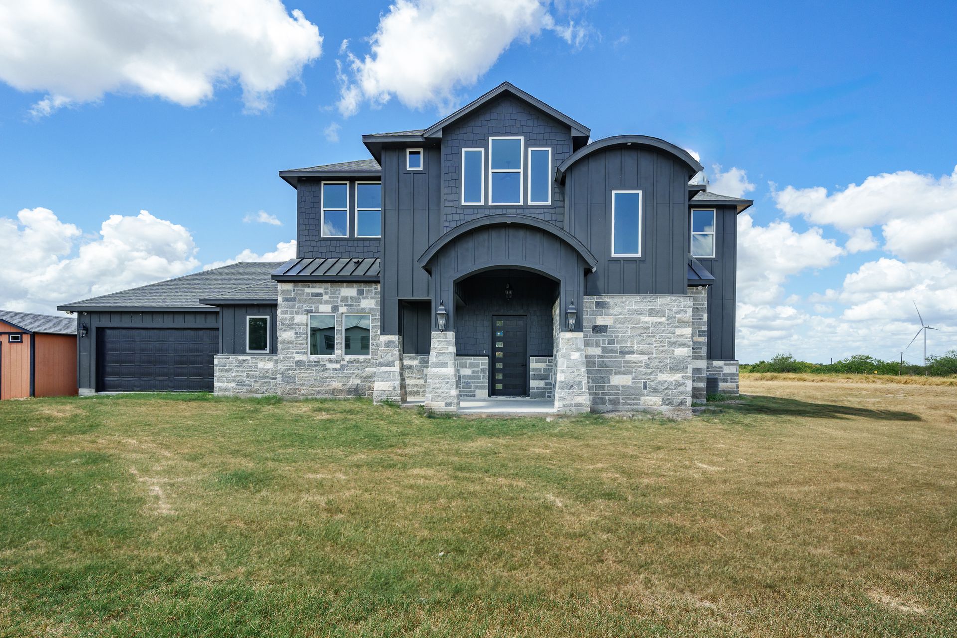 A large house with a lot of windows is sitting on top of a lush green field.