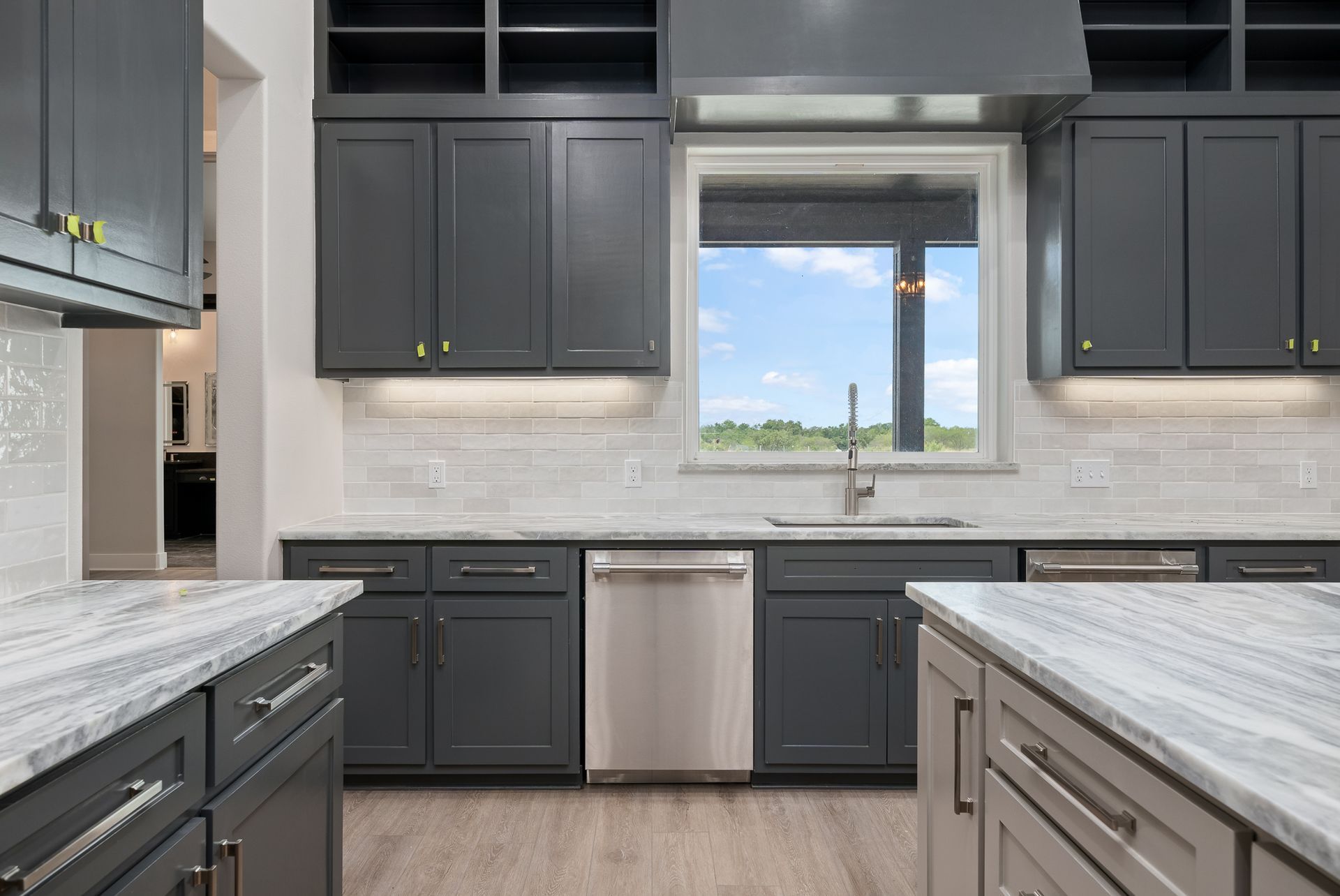 A kitchen with gray cabinets , granite counter tops , and a stainless steel dishwasher.