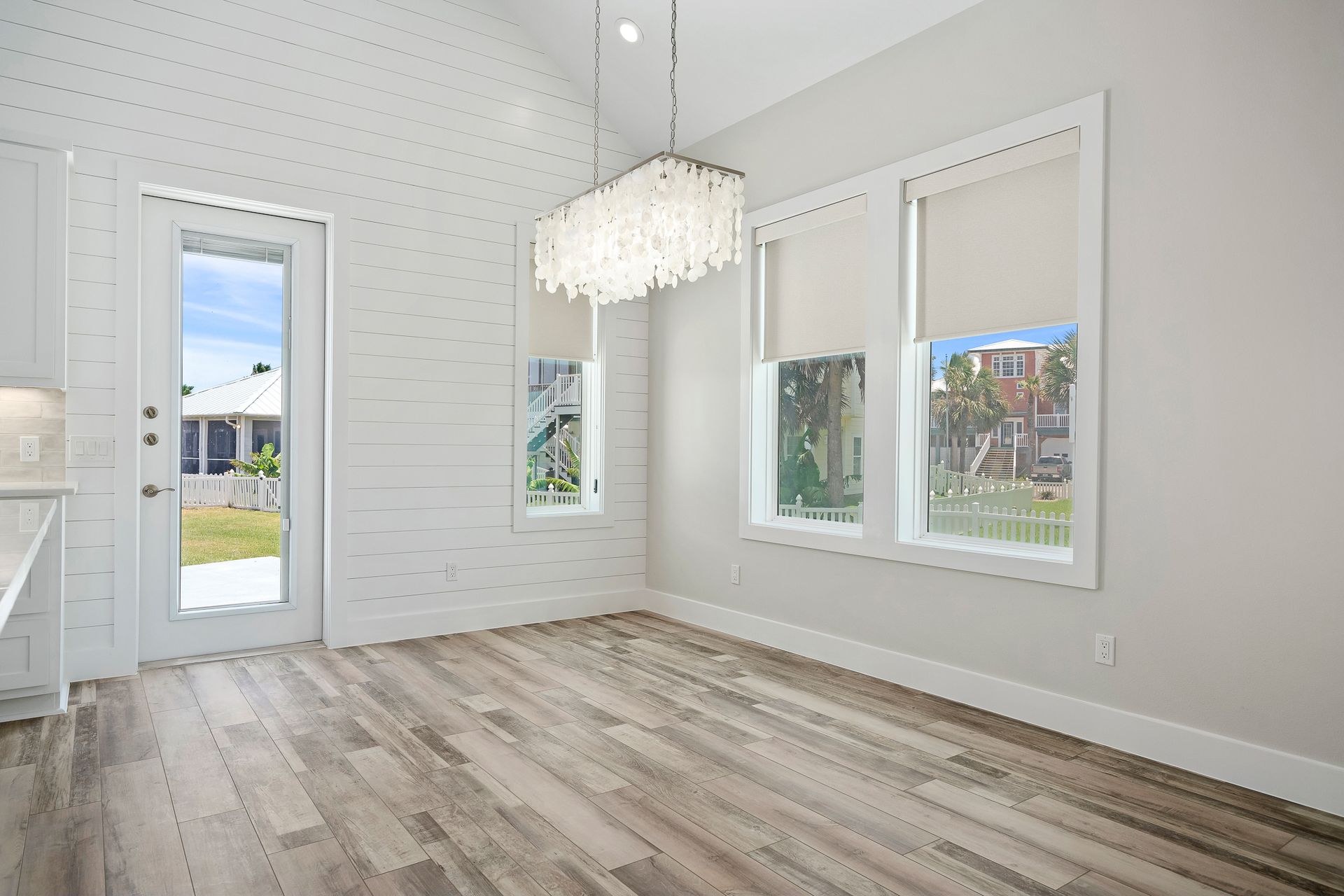 An empty dining room with hardwood floors and a chandelier hanging from the ceiling.
