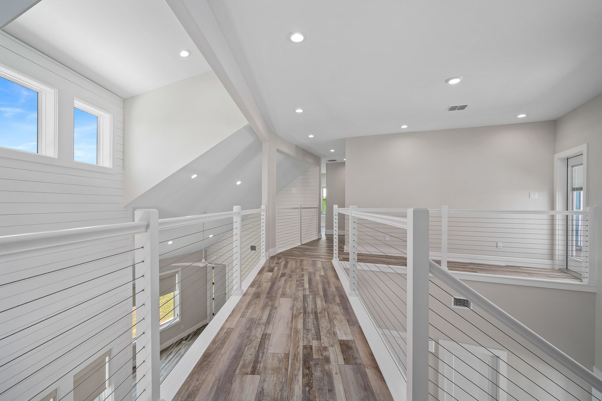 A hallway in a house with a wooden floor and a white railing.