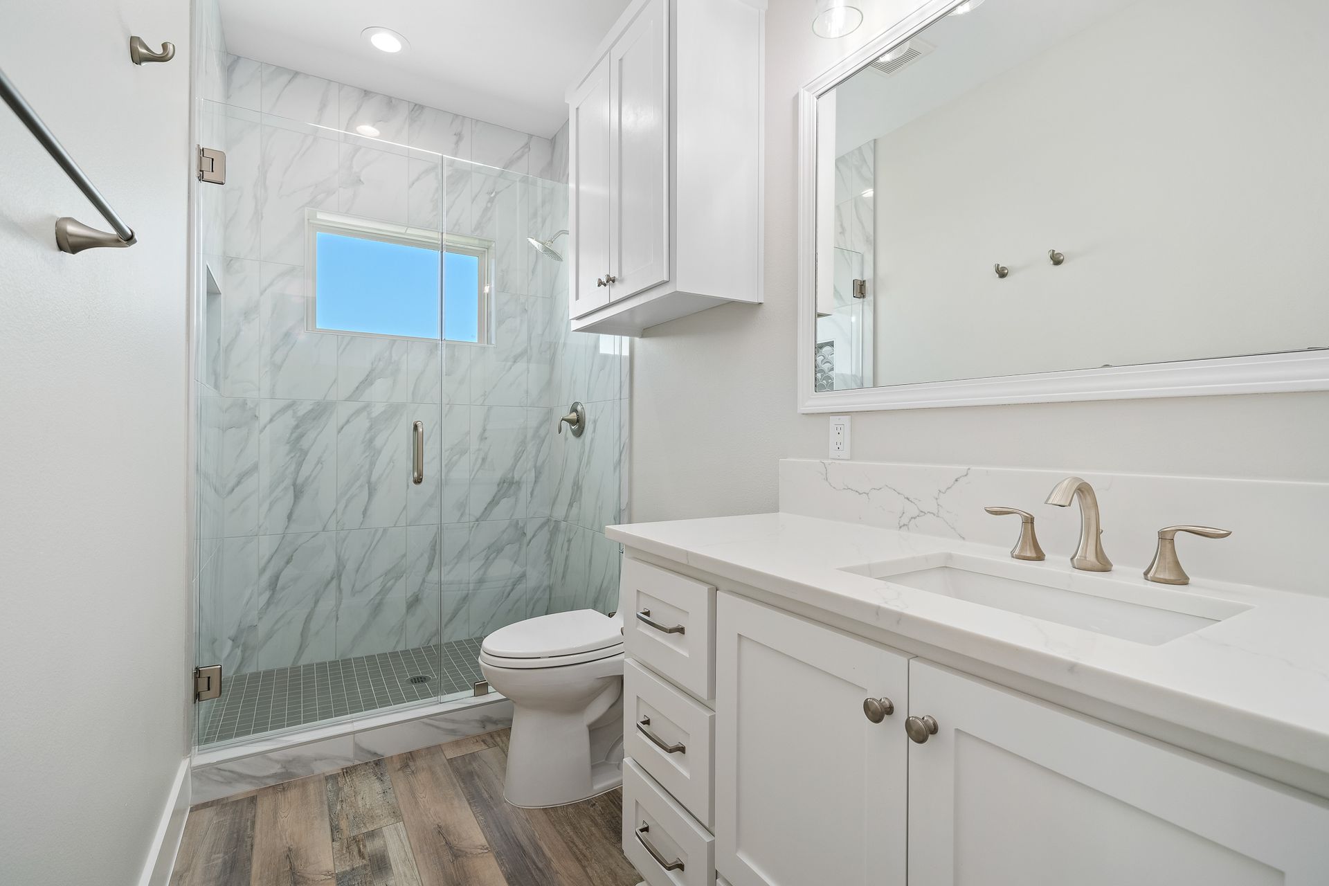 A bathroom with a toilet , sink , mirror and walk in shower.