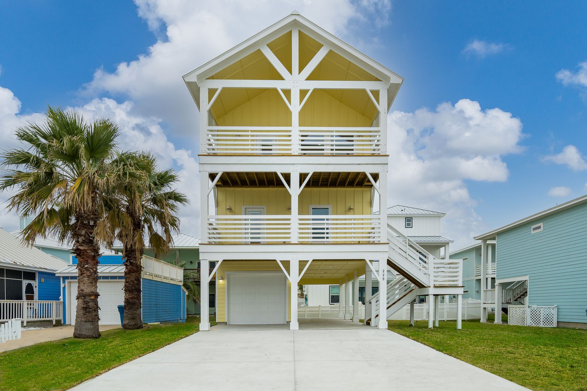 A large white house with a yellow roof is surrounded by palm trees.