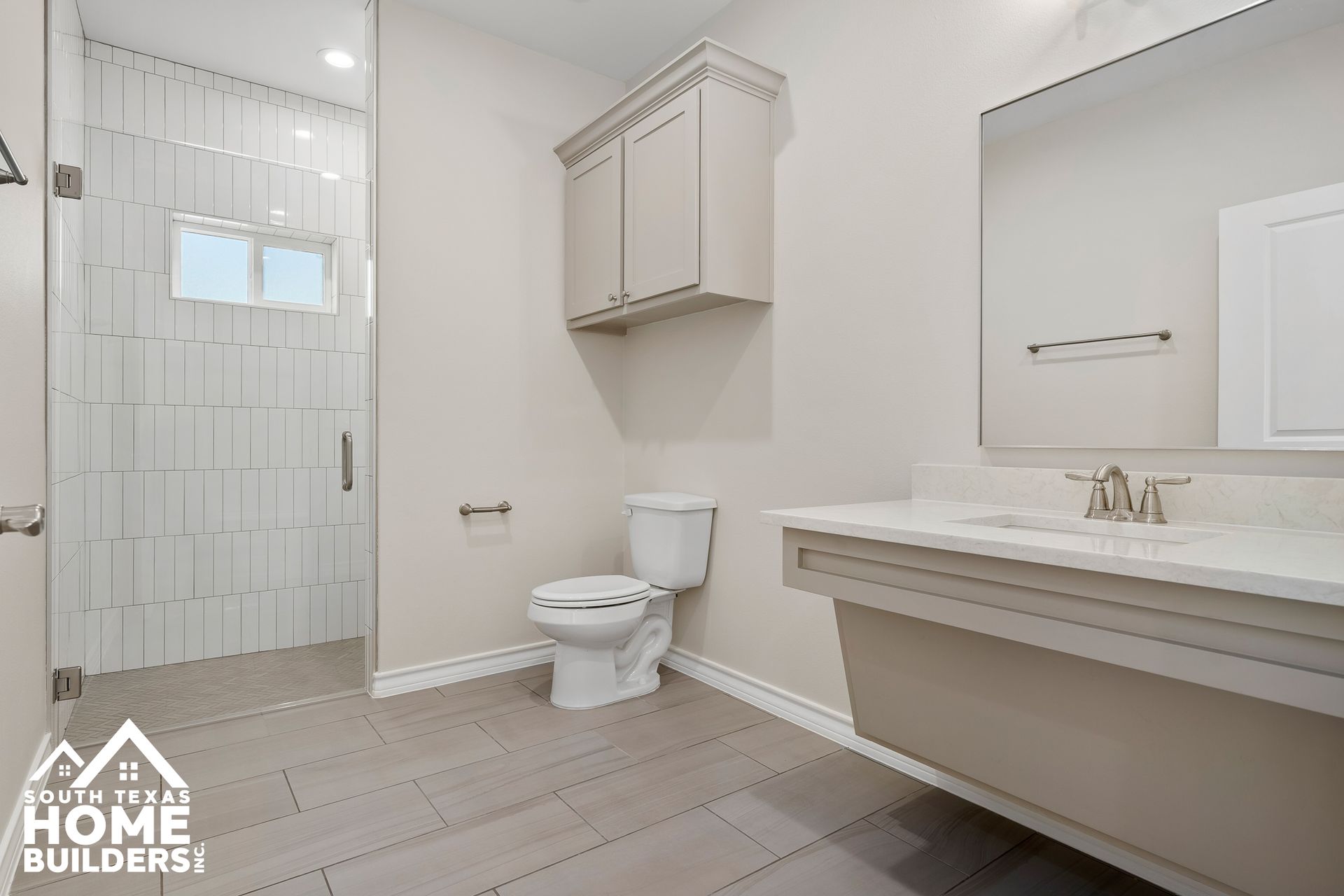 Bathroom with a glass shower, toilet, floating vanity, and upper cabinet; neutral colors.