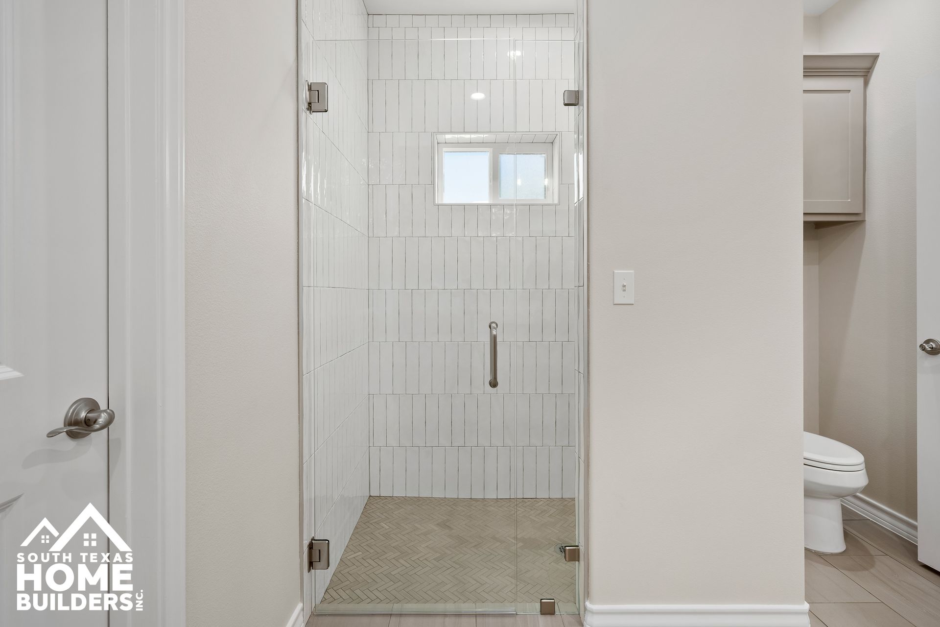 Bathroom with glass shower door, white tile, small window, and light-colored walls.