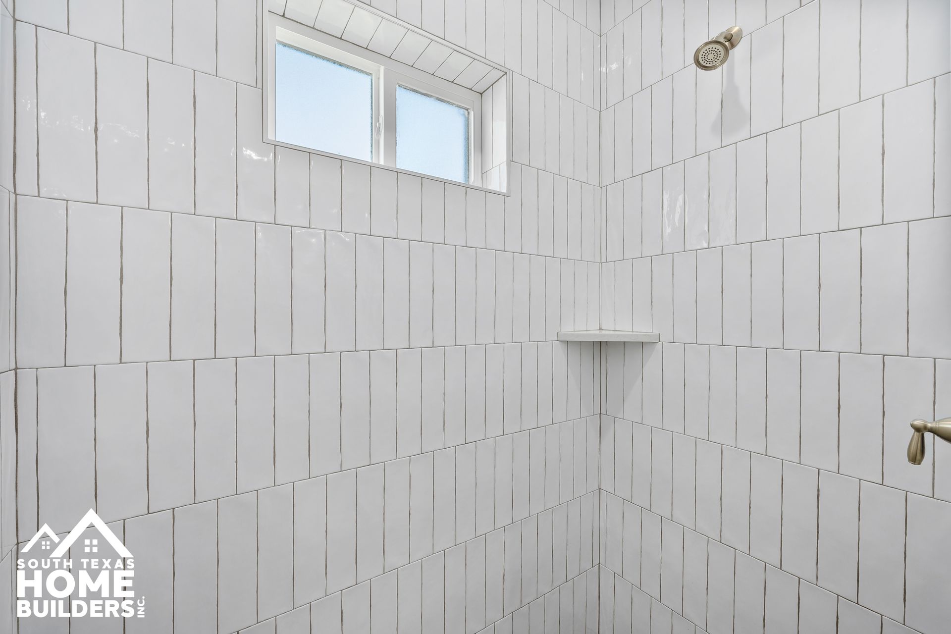 White tiled shower with a small window, built-in shelf, and showerhead.