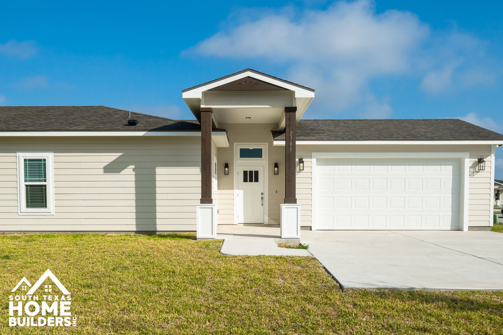 Beige house with white door, garage, and brown pillars on a blue sky day.