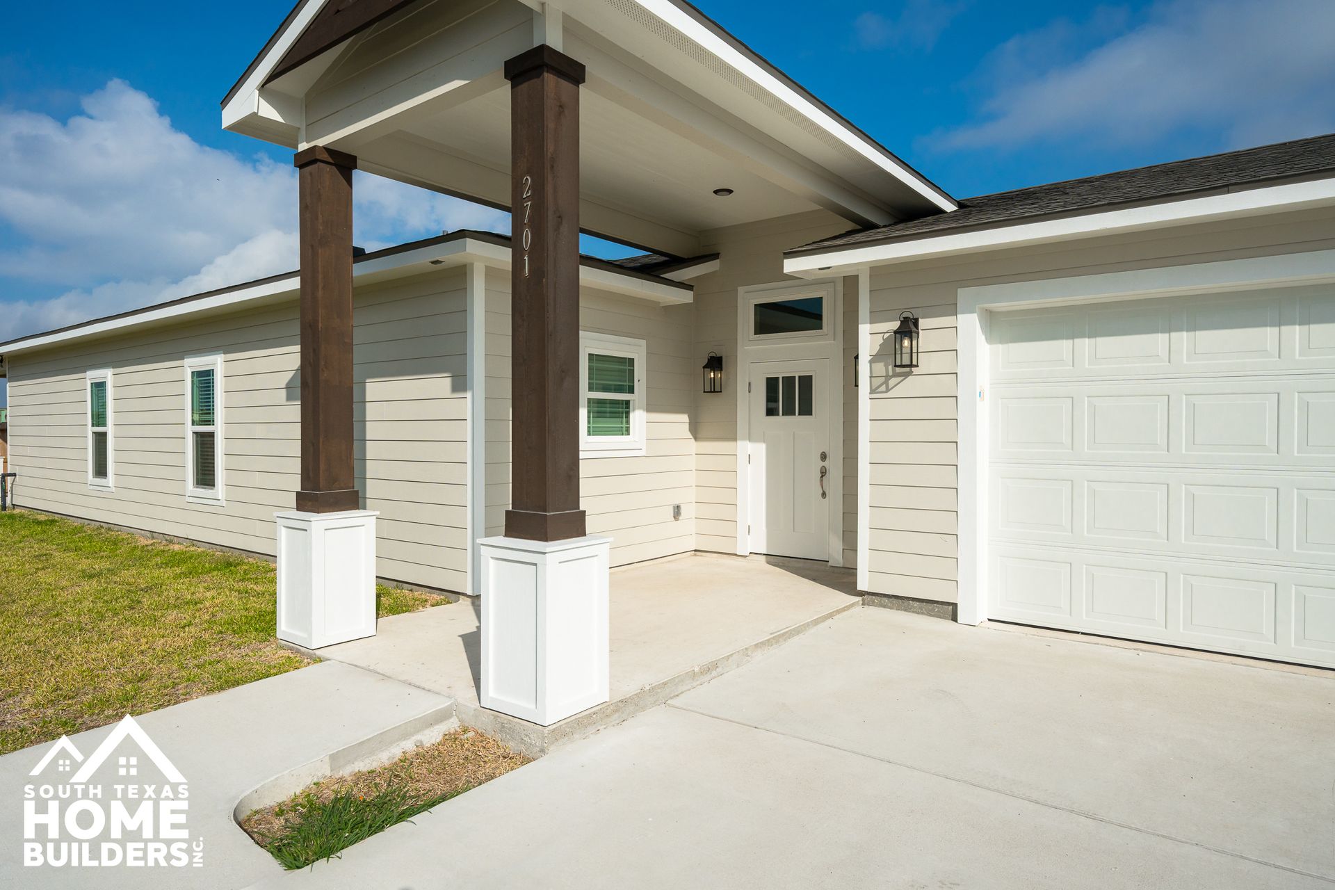 Exterior of a beige house with a covered porch supported by dark brown columns. Concrete walkway and white garage door.