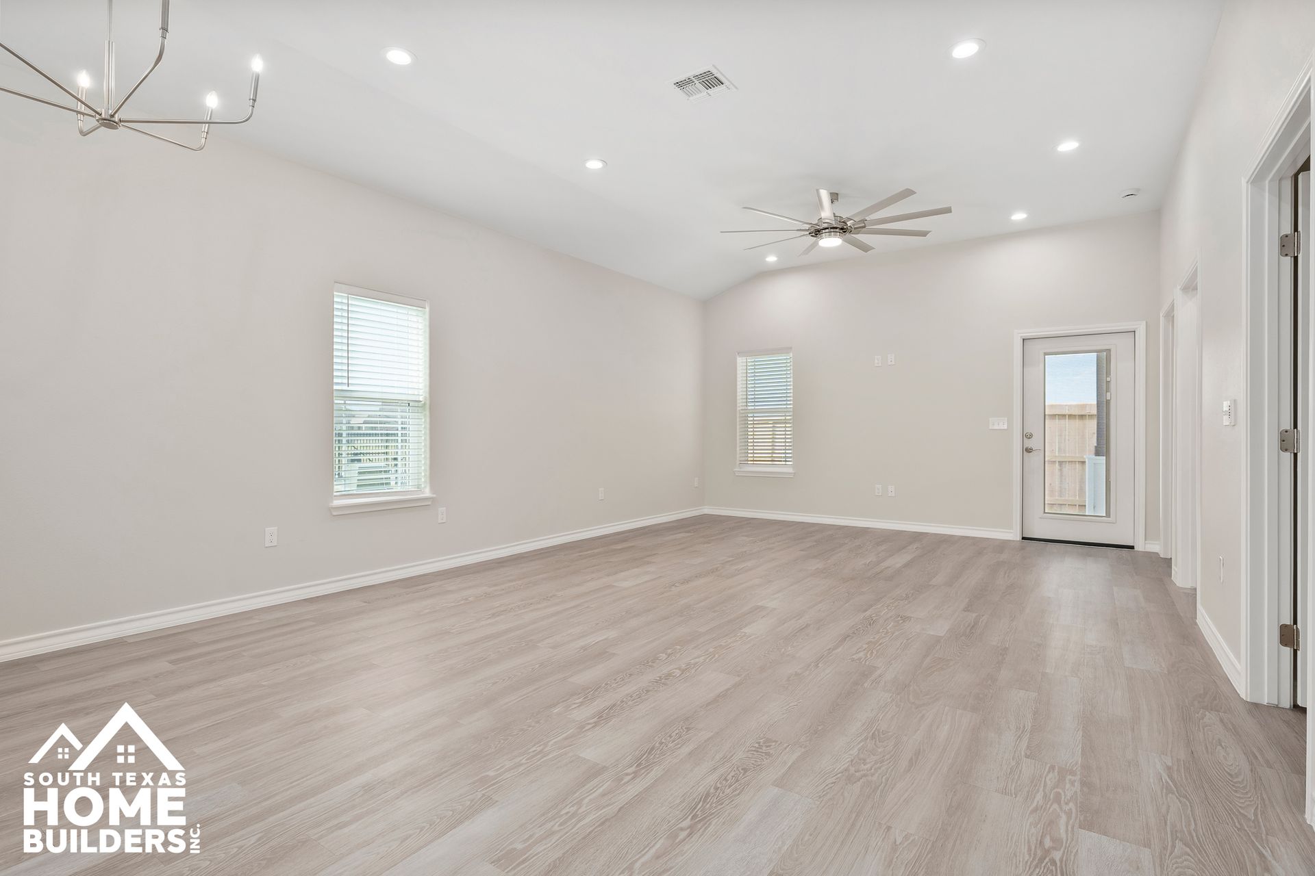 Spacious, empty room with light gray walls, flooring, and a door to the outside.