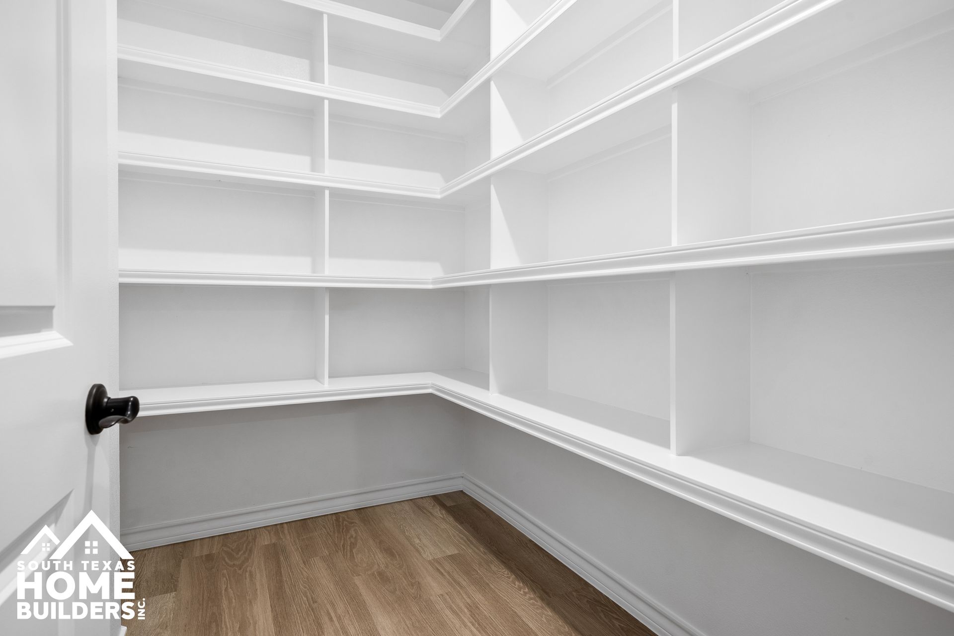 Empty white pantry with multiple shelves. Light brown flooring and black doorknob.