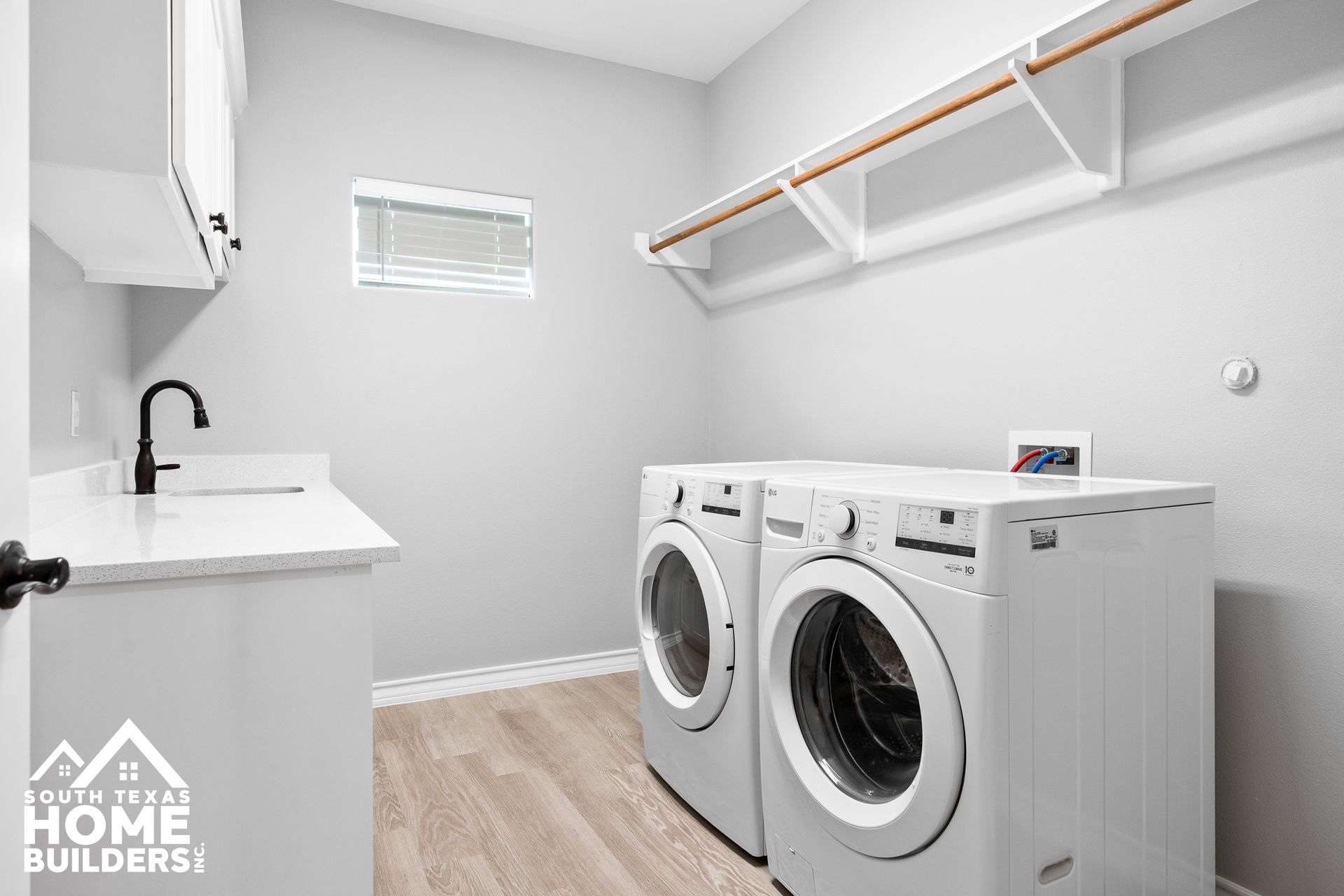 Laundry room with white appliances, cabinets, and light gray walls. Includes a sink and clothes rack.