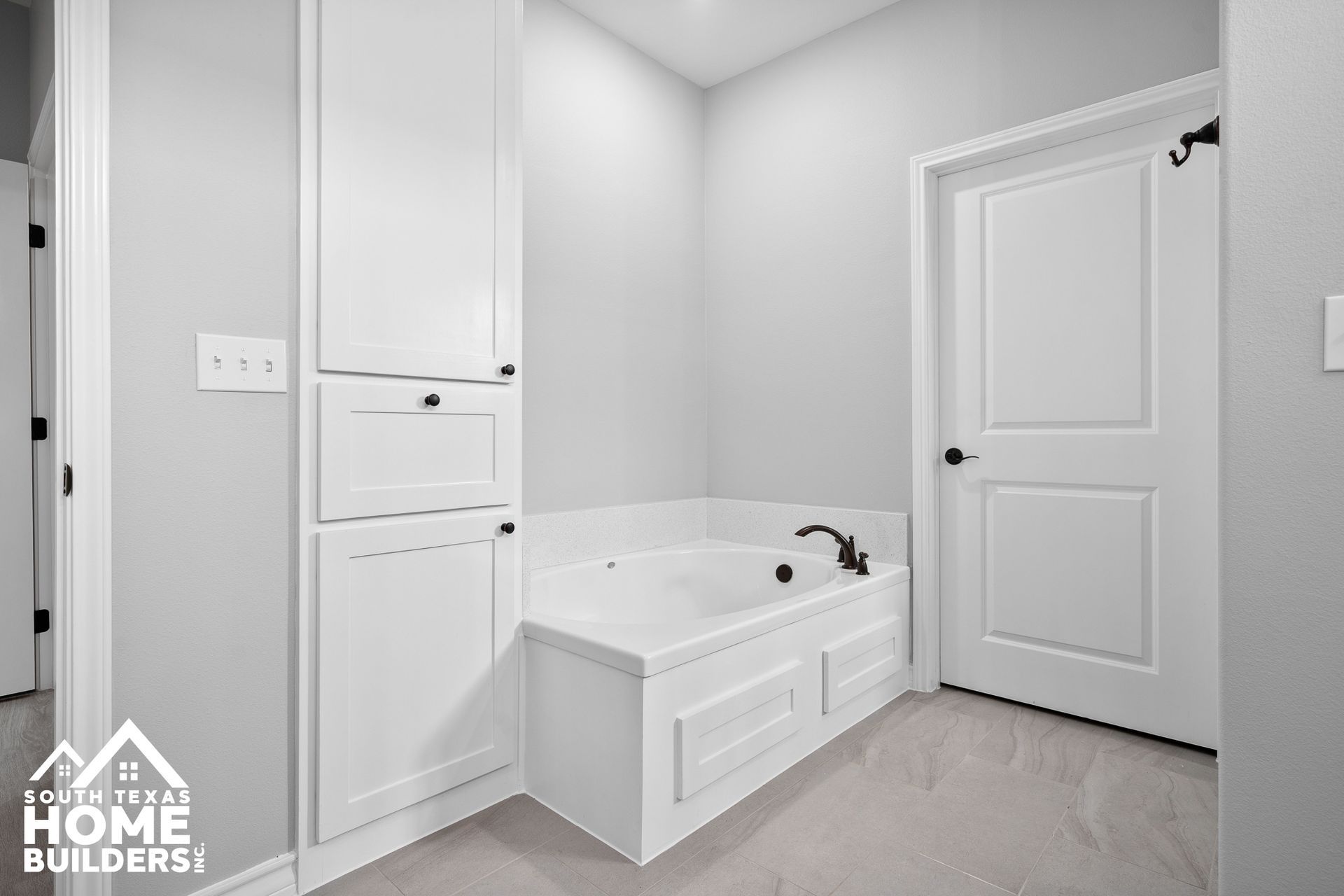 White bathroom with built-in tub, storage cabinets, and a closed door.
