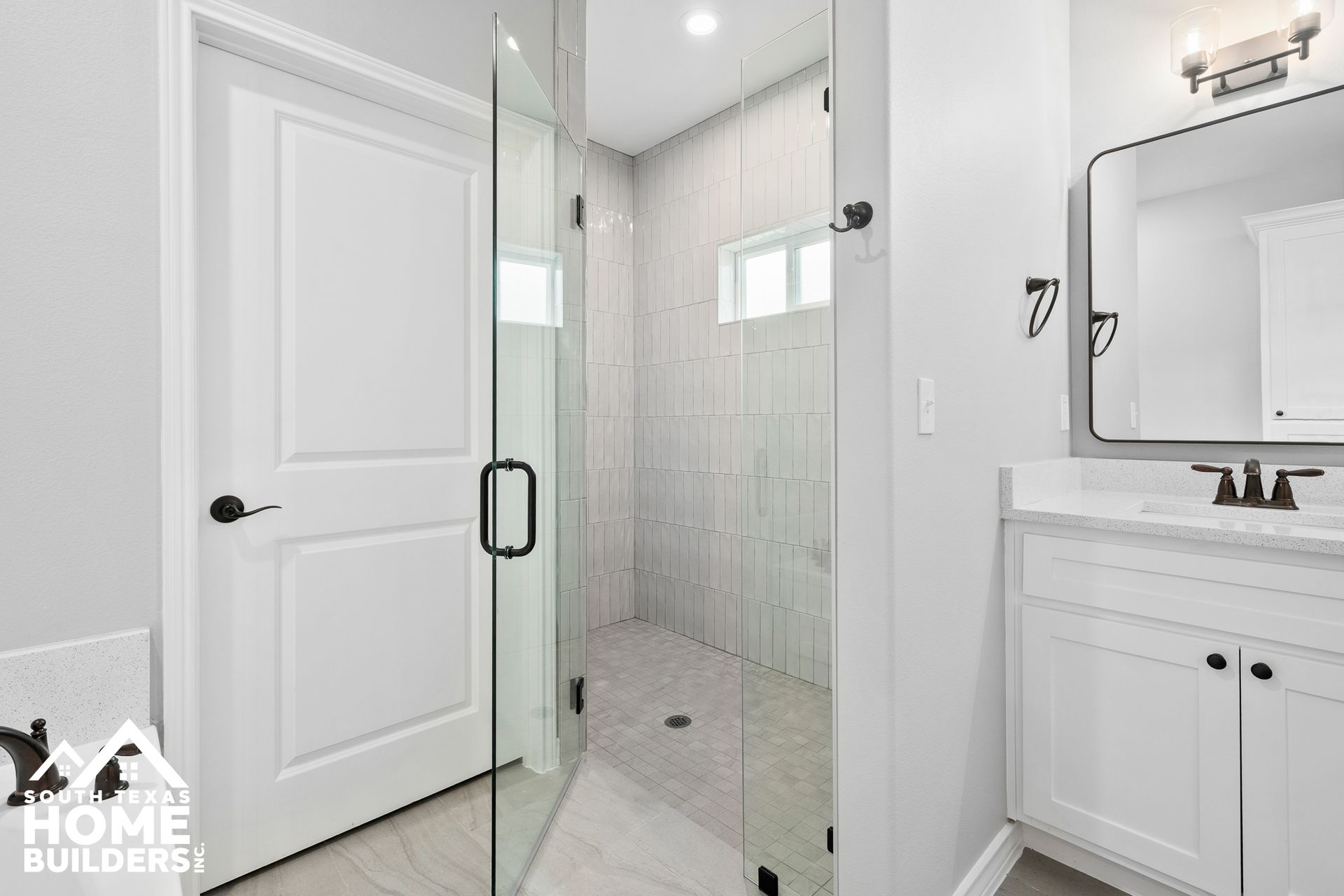 Modern bathroom with a glass shower, white cabinets, and a rectangular mirror.