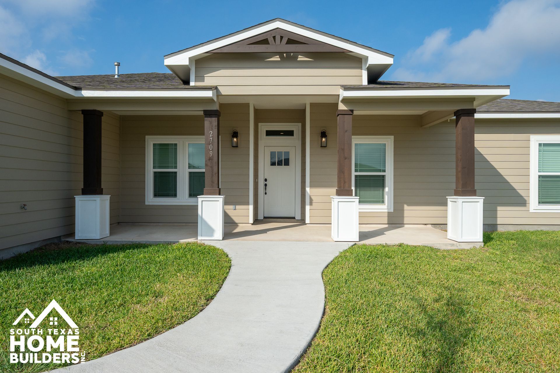 Beige home with a covered porch and brown columns; concrete pathway leads to the white front door.