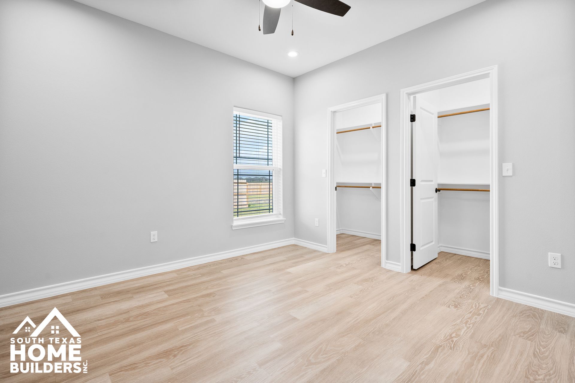 Empty bedroom with light wood floors, gray walls, white trim, two closets, and a window.
