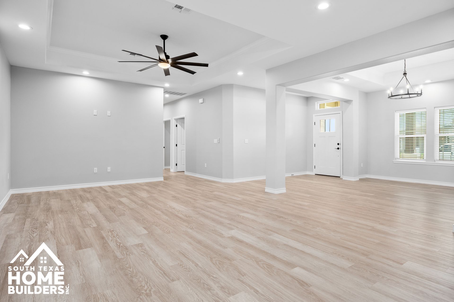 Spacious living room with light wood floors, gray walls, ceiling fan, and large windows.