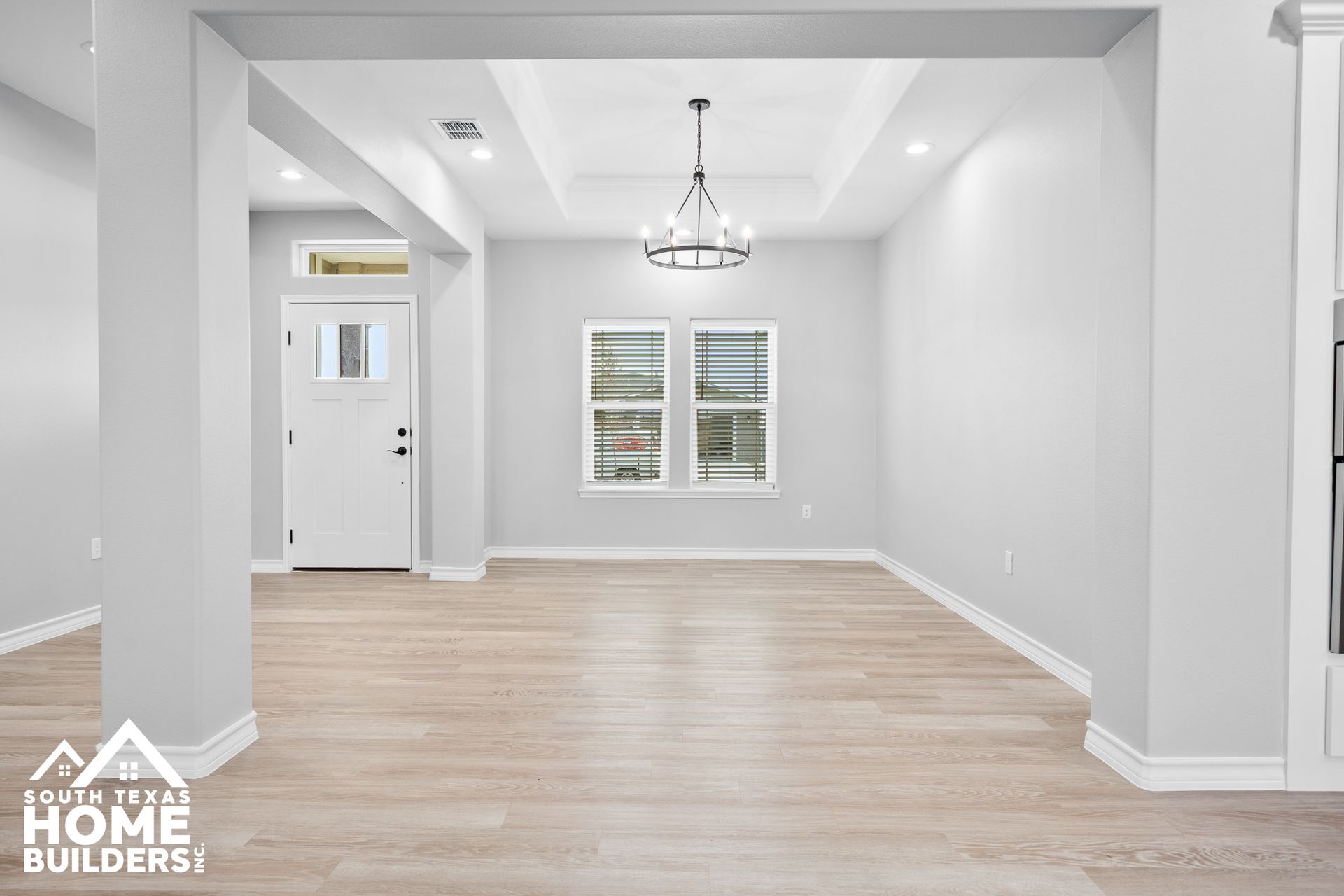 Empty, bright dining room with pale wood floors, white walls, and a chandelier.