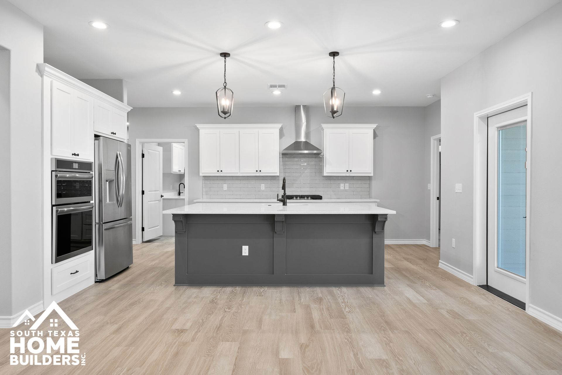 Modern kitchen with white cabinets, gray island, stainless steel appliances, and wood flooring.