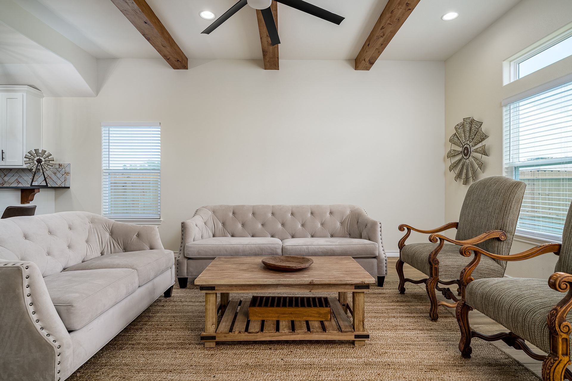 A living room with two couches , two chairs , a coffee table and a ceiling fan.