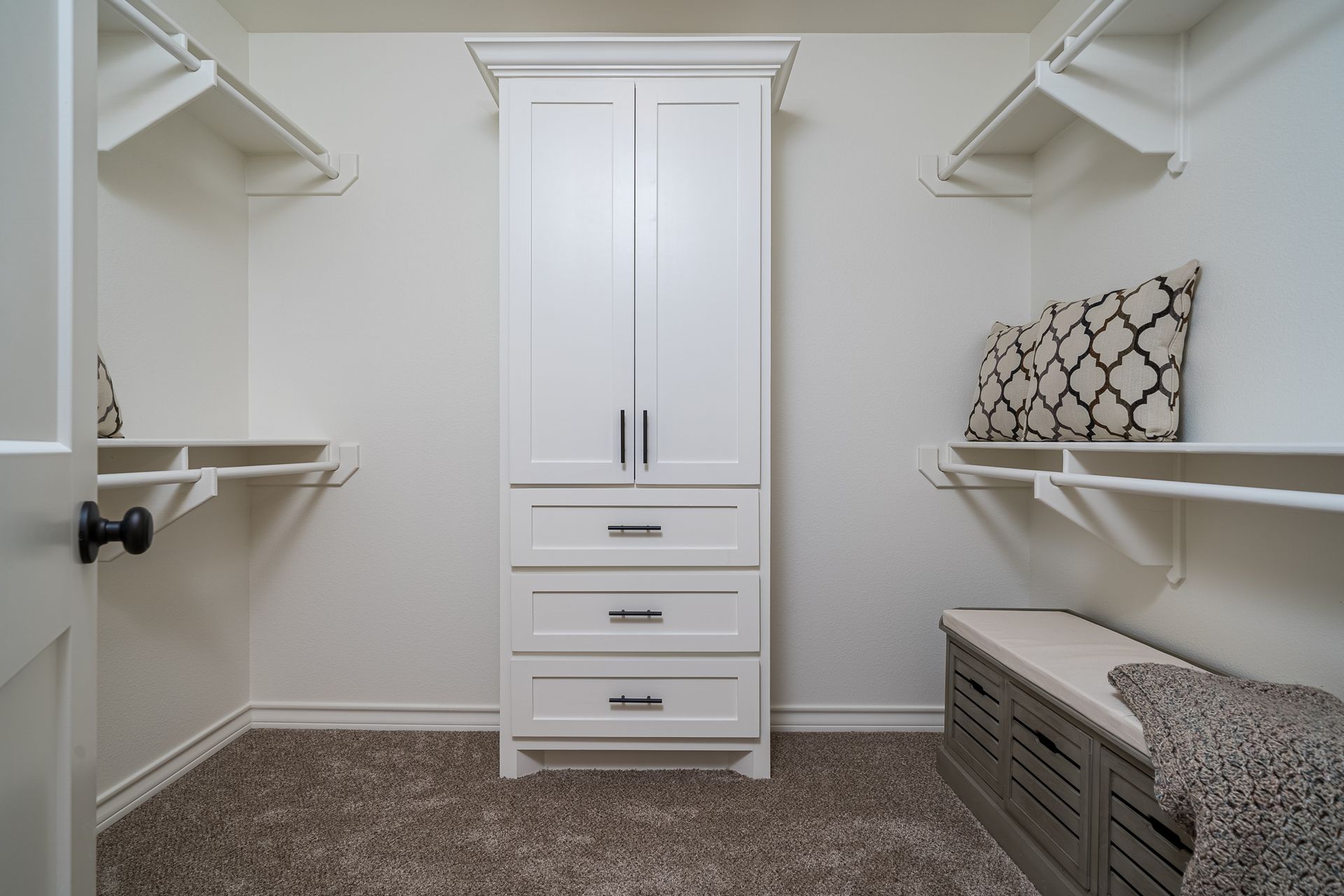 A walk in closet with a dresser , shelves , and a bench.