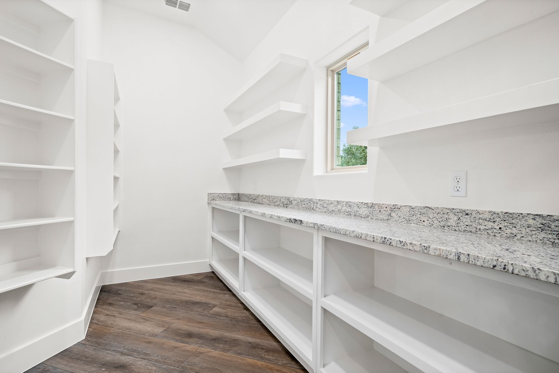 An empty pantry with lots of shelves and a window.