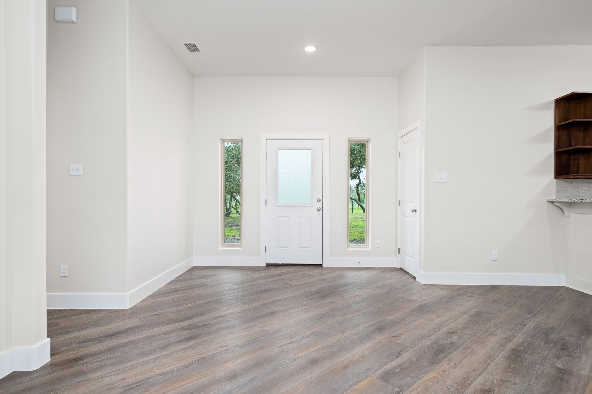 An empty living room with hardwood floors and white walls.