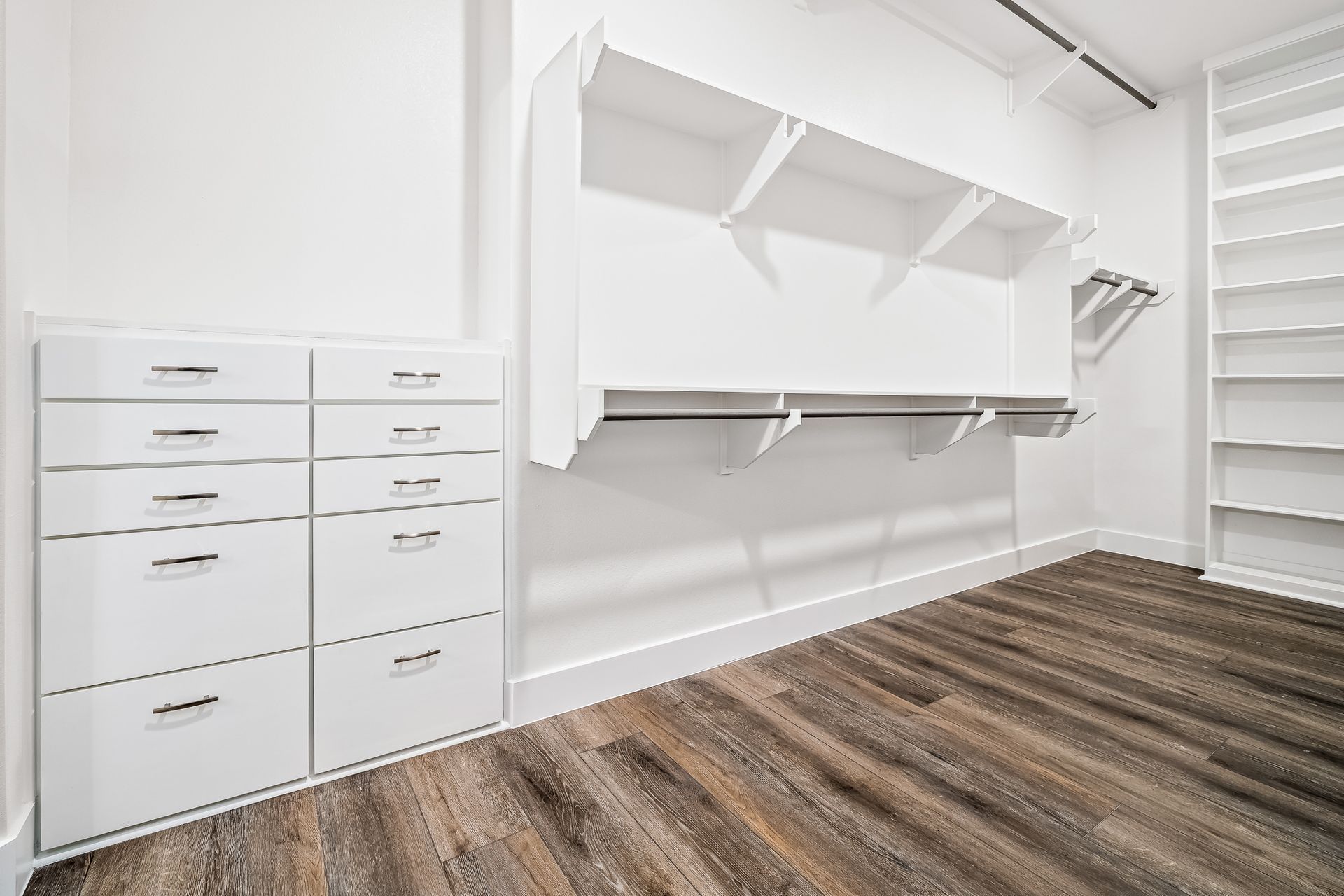 An empty walk in closet with wooden floors and white shelves.
