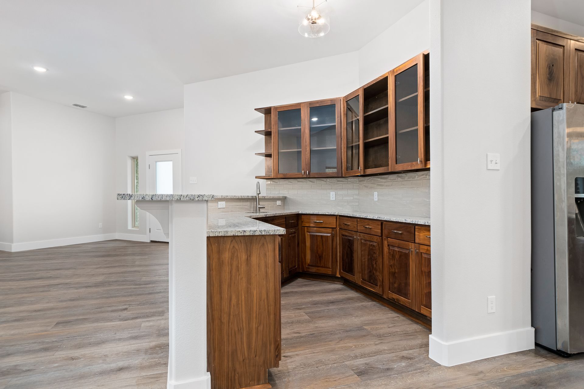 An empty kitchen with wooden cabinets and a stainless steel refrigerator.