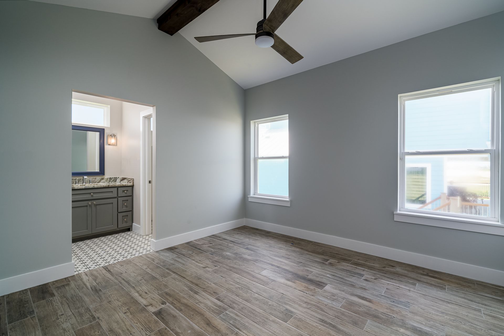 An empty room with a ceiling fan and three windows.