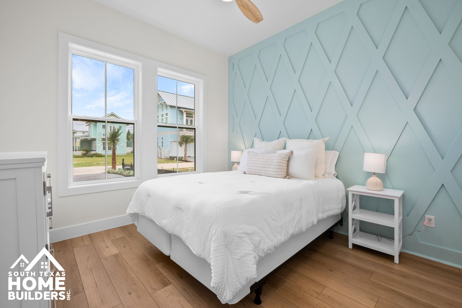 Bedroom with a light blue accent wall, white bedding, and hardwood floors.