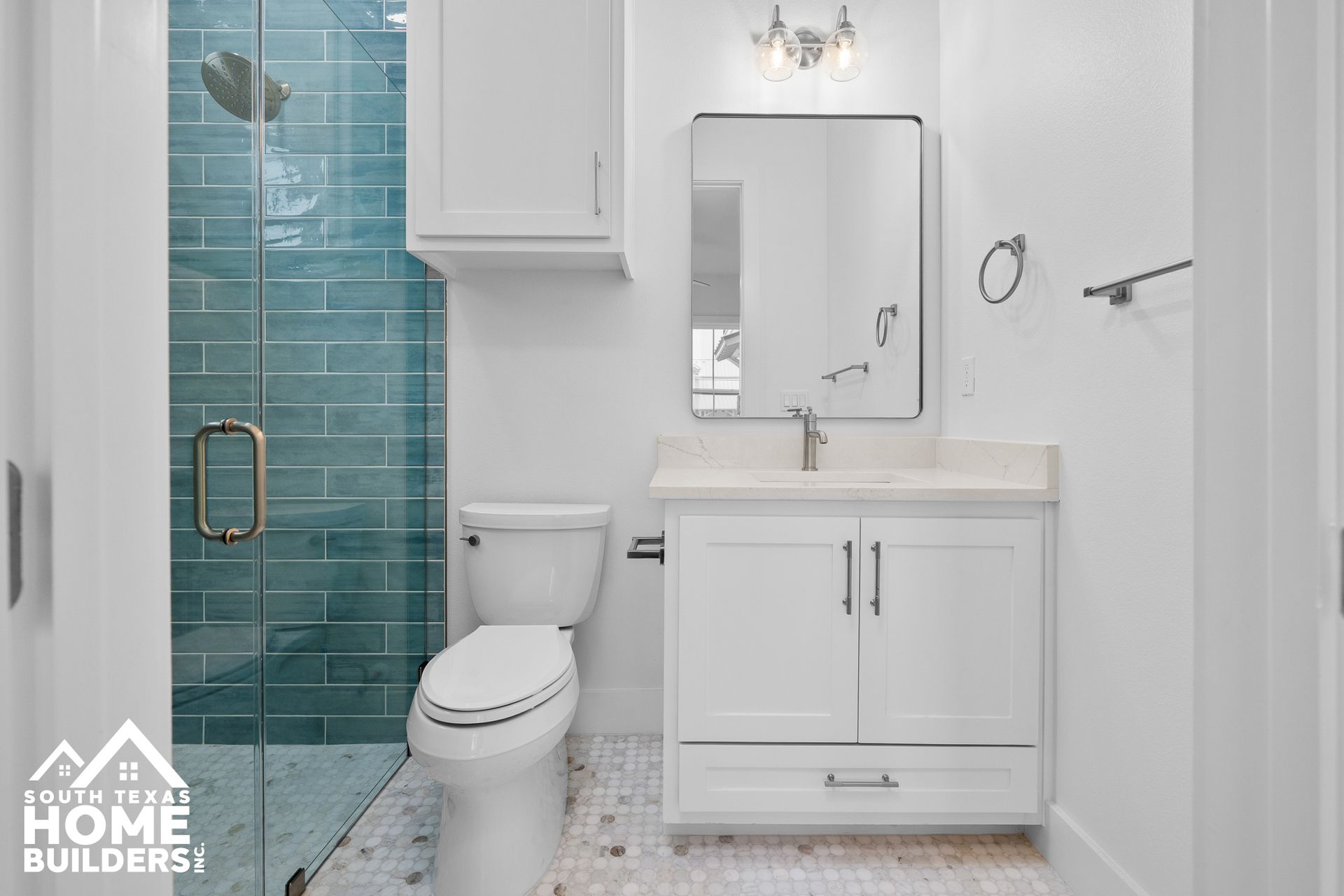 White bathroom with blue tiled shower, vanity, and toilet.