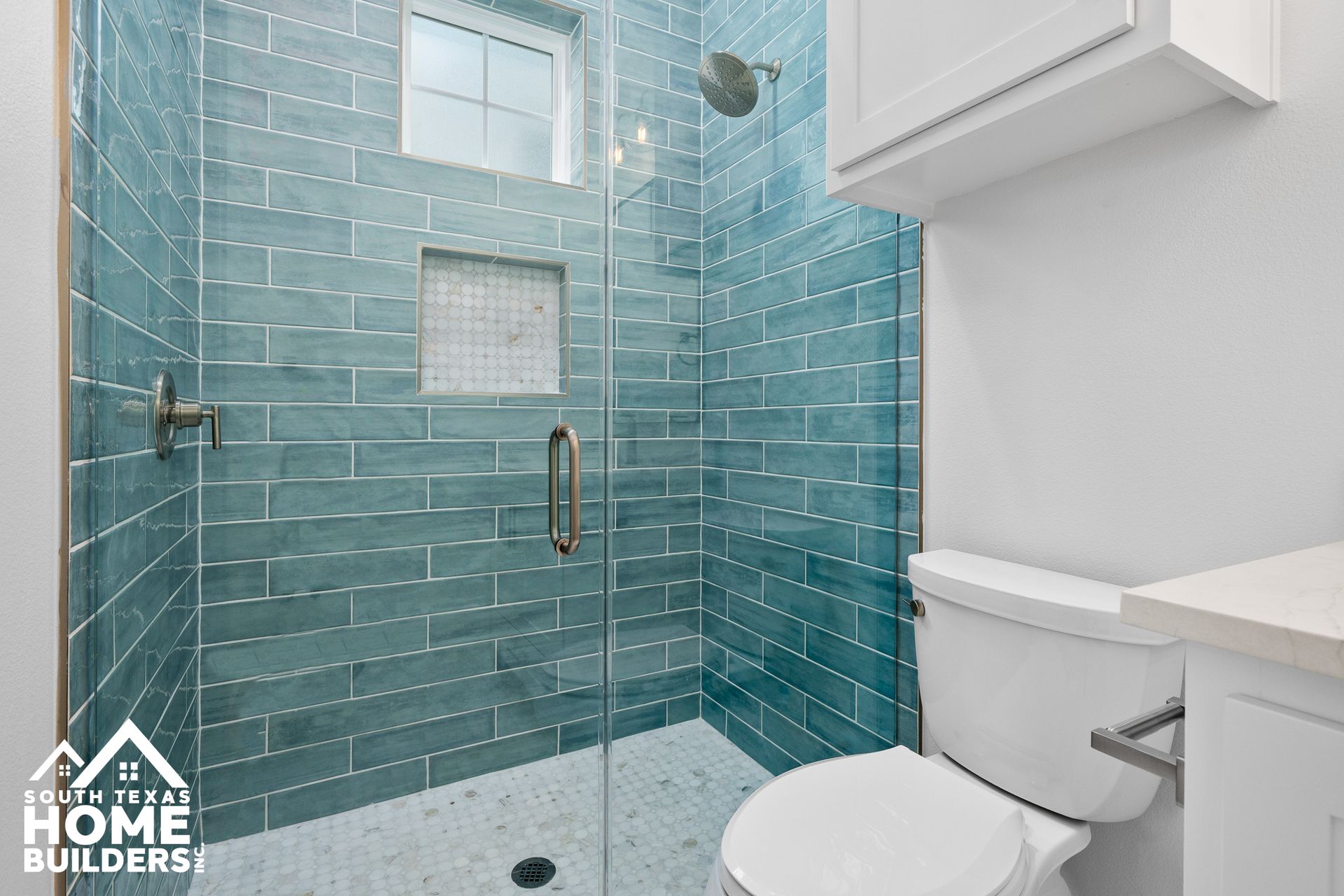 Blue tiled shower with glass door and white toilet in a bathroom.