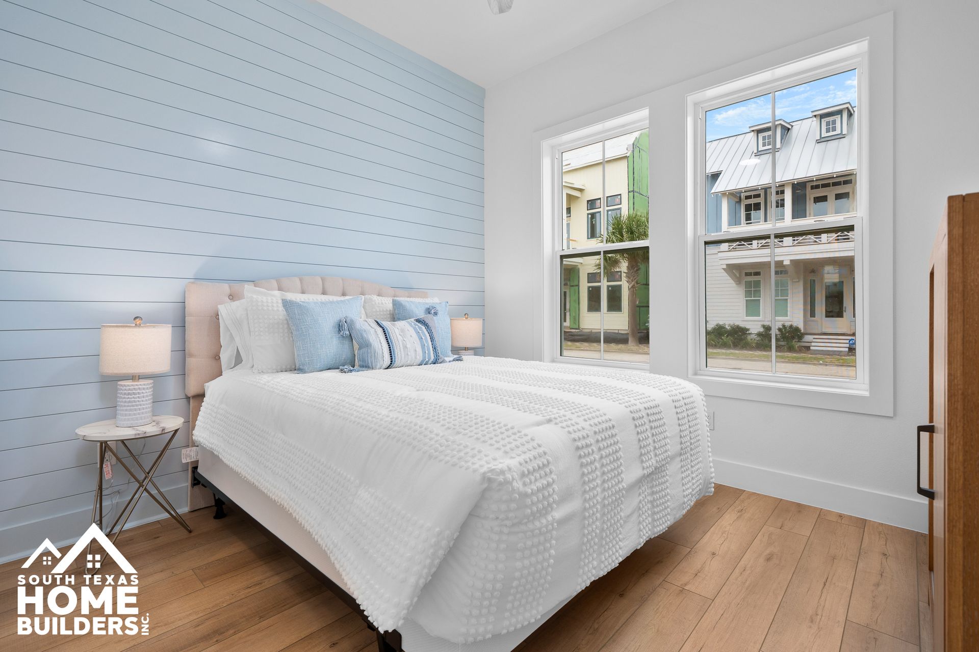 Bedroom with blue shiplap accent wall, white bedding, and two windows.