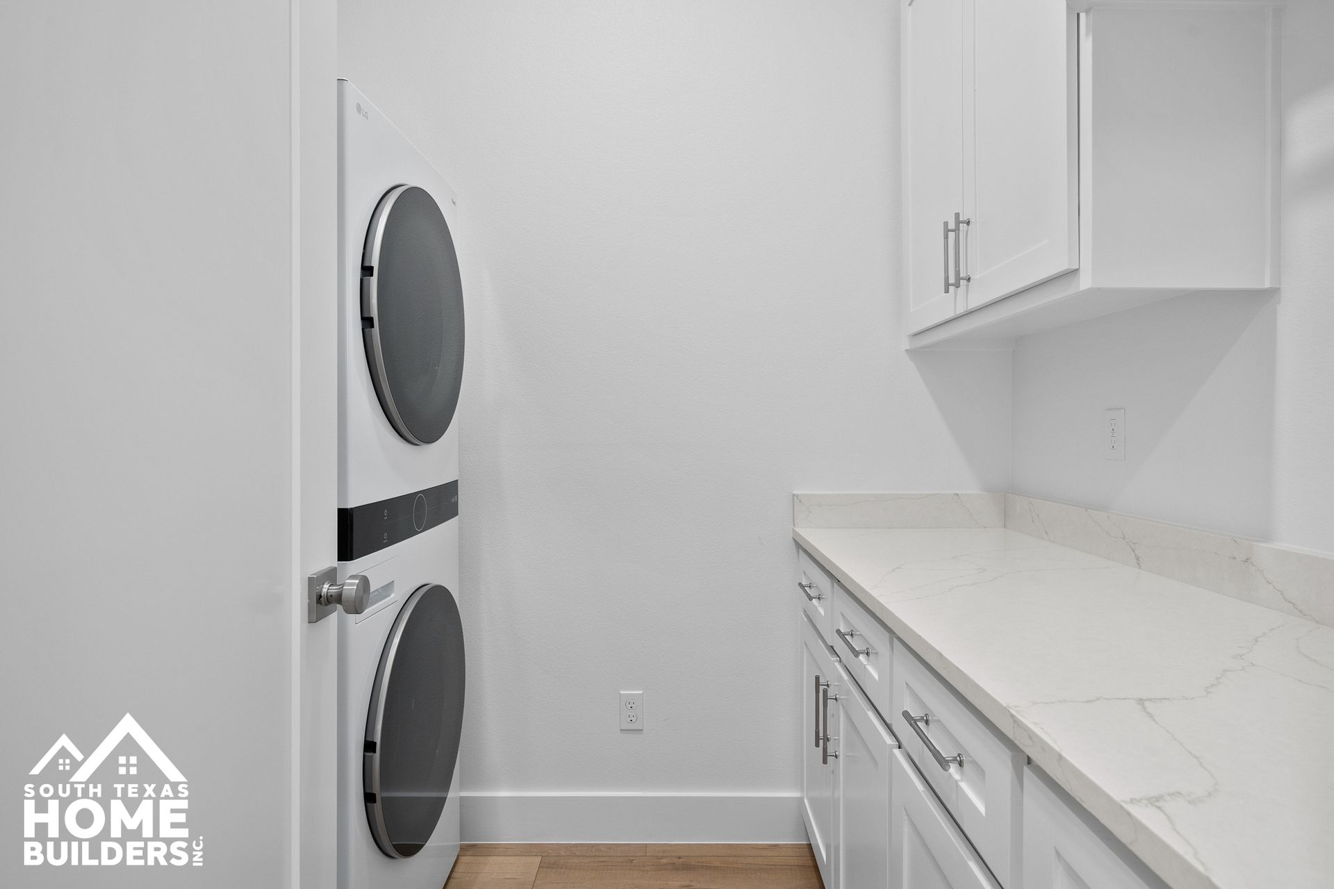 White laundry room with stacked washer and dryer, cabinets, and countertop.