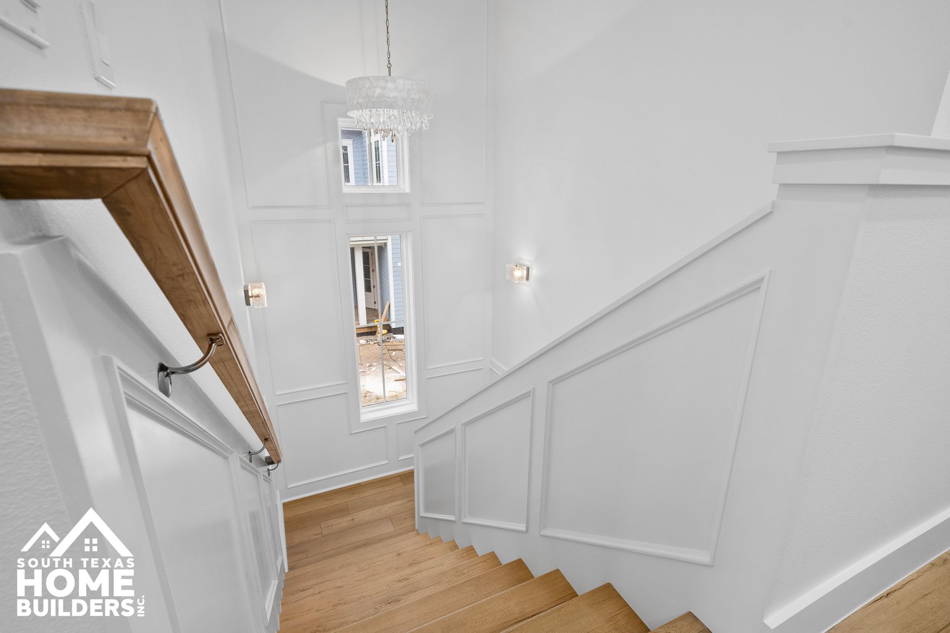 Stairwell with white walls, wood trim, and a chandelier, leading to a room with natural light.