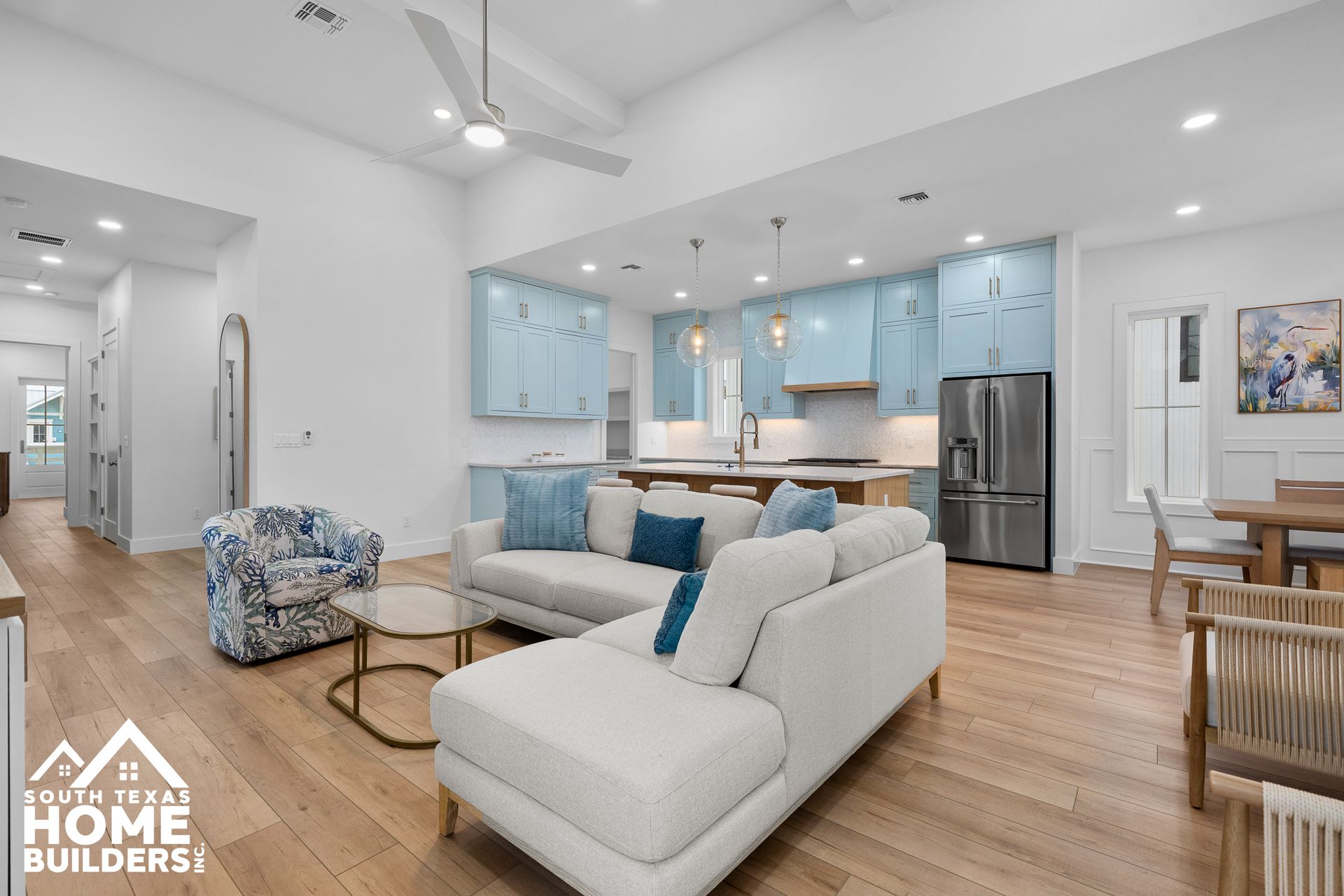 Open-concept living space with light wood floors, blue kitchen cabinets, and white sectional sofa.
