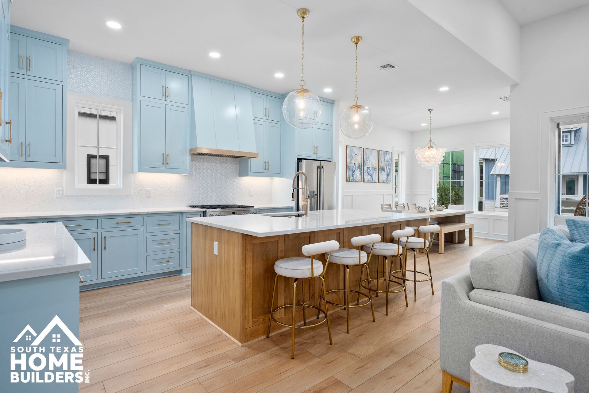 Open-concept kitchen with light blue cabinets, wood island, and gold accents.