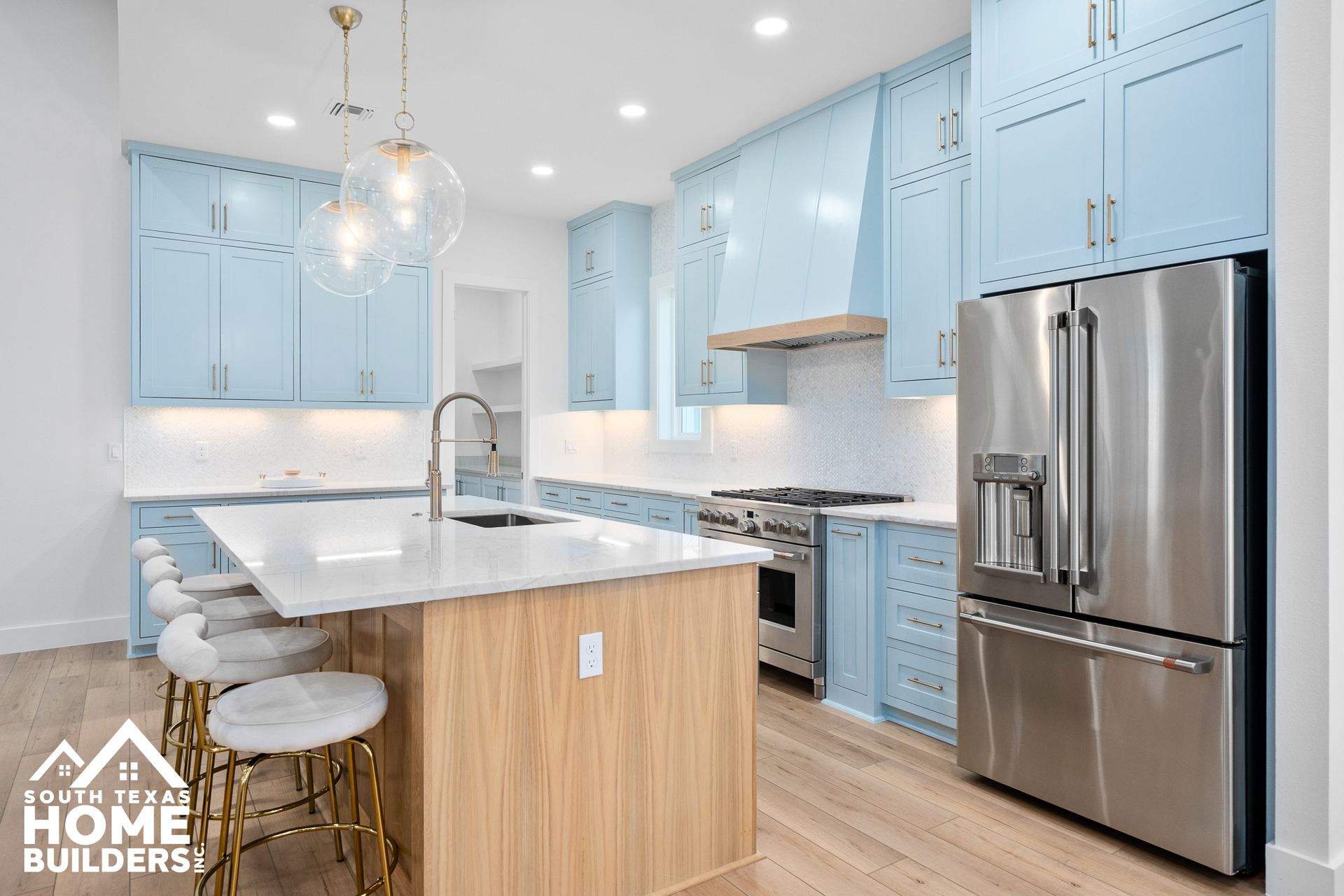 Light blue kitchen with island, stainless steel appliances, and white countertops.