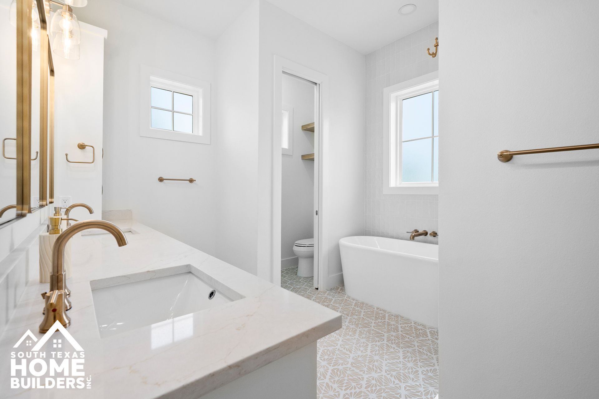 Bright white modern bathroom with gold fixtures, a soaking tub, and a vanity with two sinks.