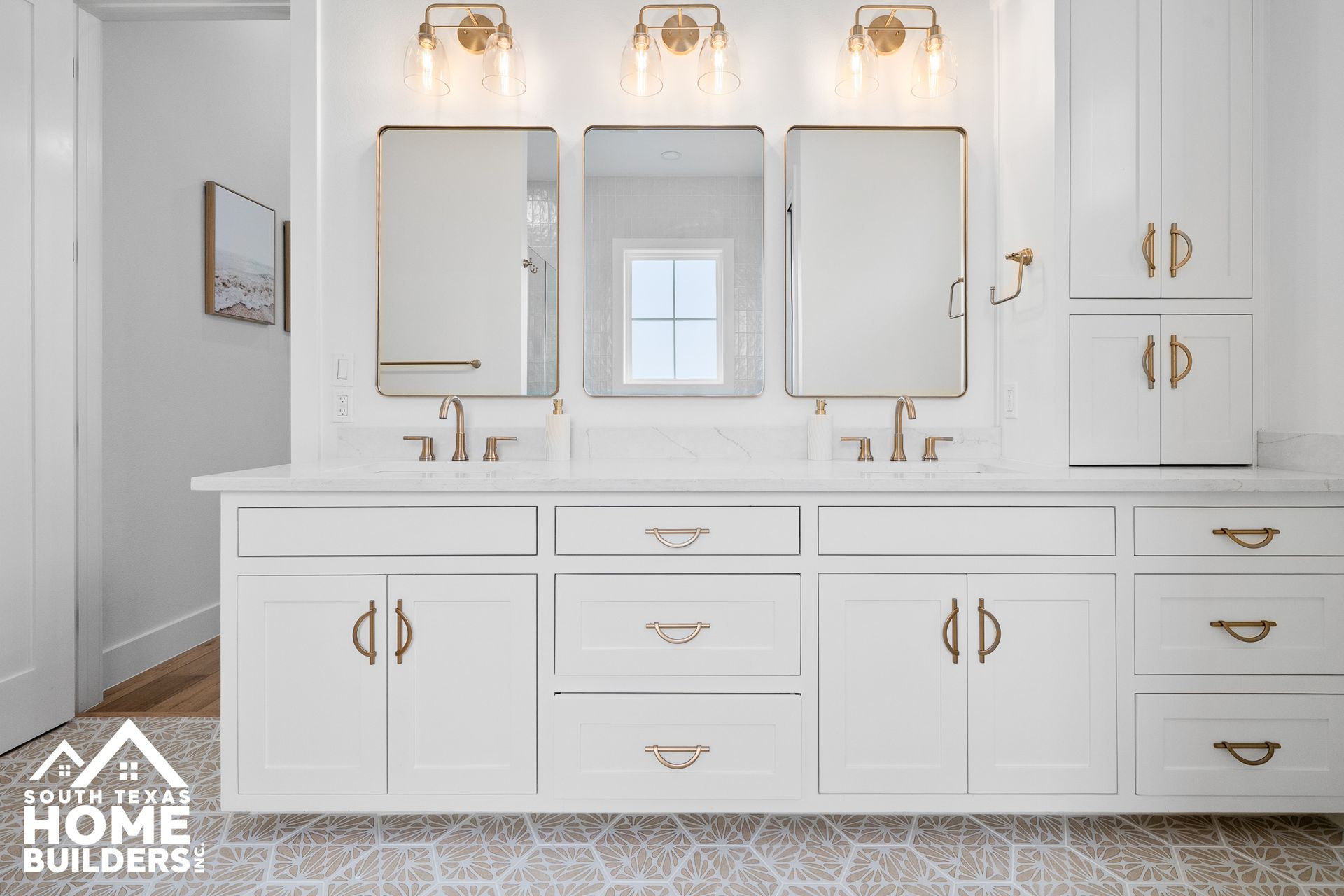 White bathroom vanity with three mirrors, gold fixtures, and patterned flooring.