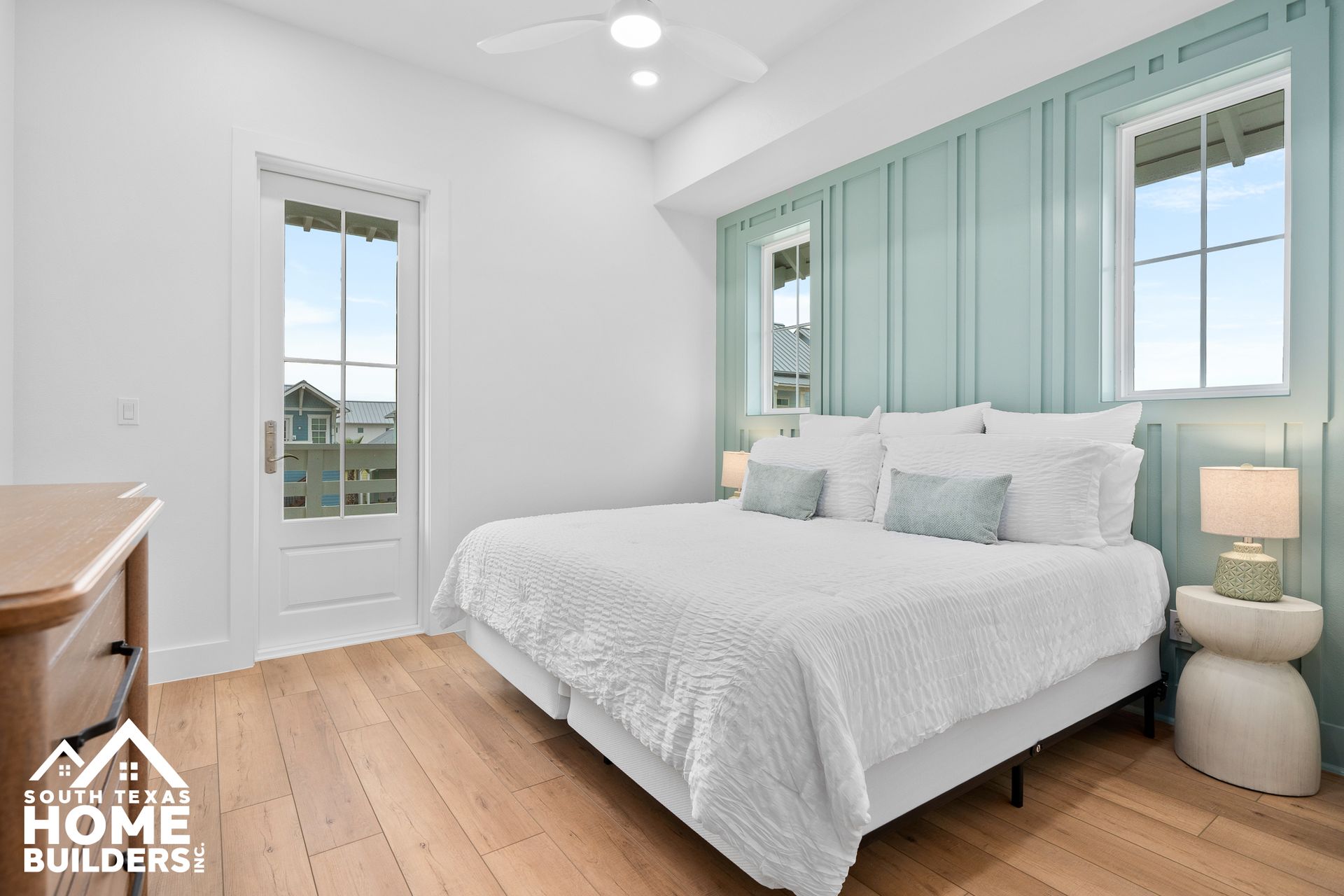 Bedroom with white bedding, turquoise accent wall, wooden floors, and natural light.