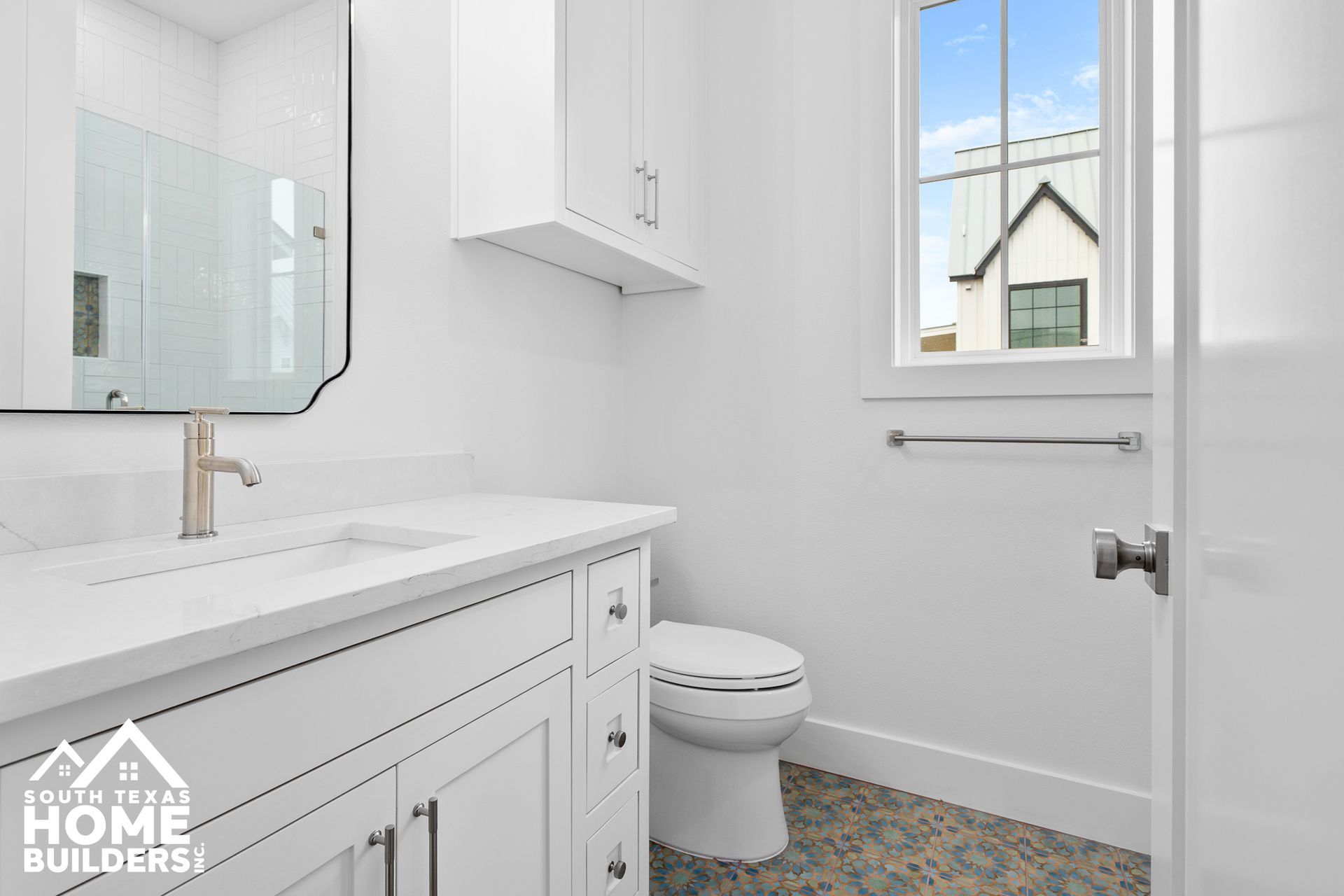 White bathroom with vanity, toilet, and window overlooking a house.