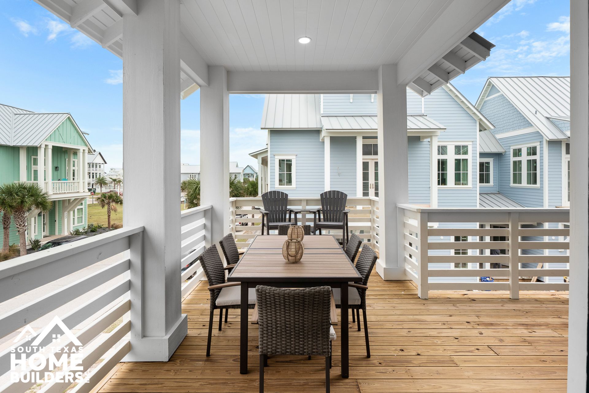 Covered outdoor dining area with table and chairs, overlooking other houses.