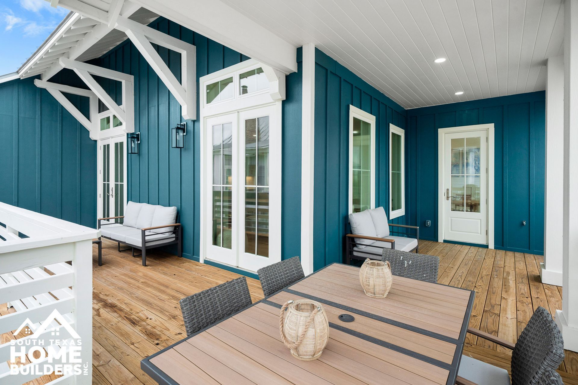 Covered outdoor deck with blue siding, white trim, and wooden floor. Table and seating present.