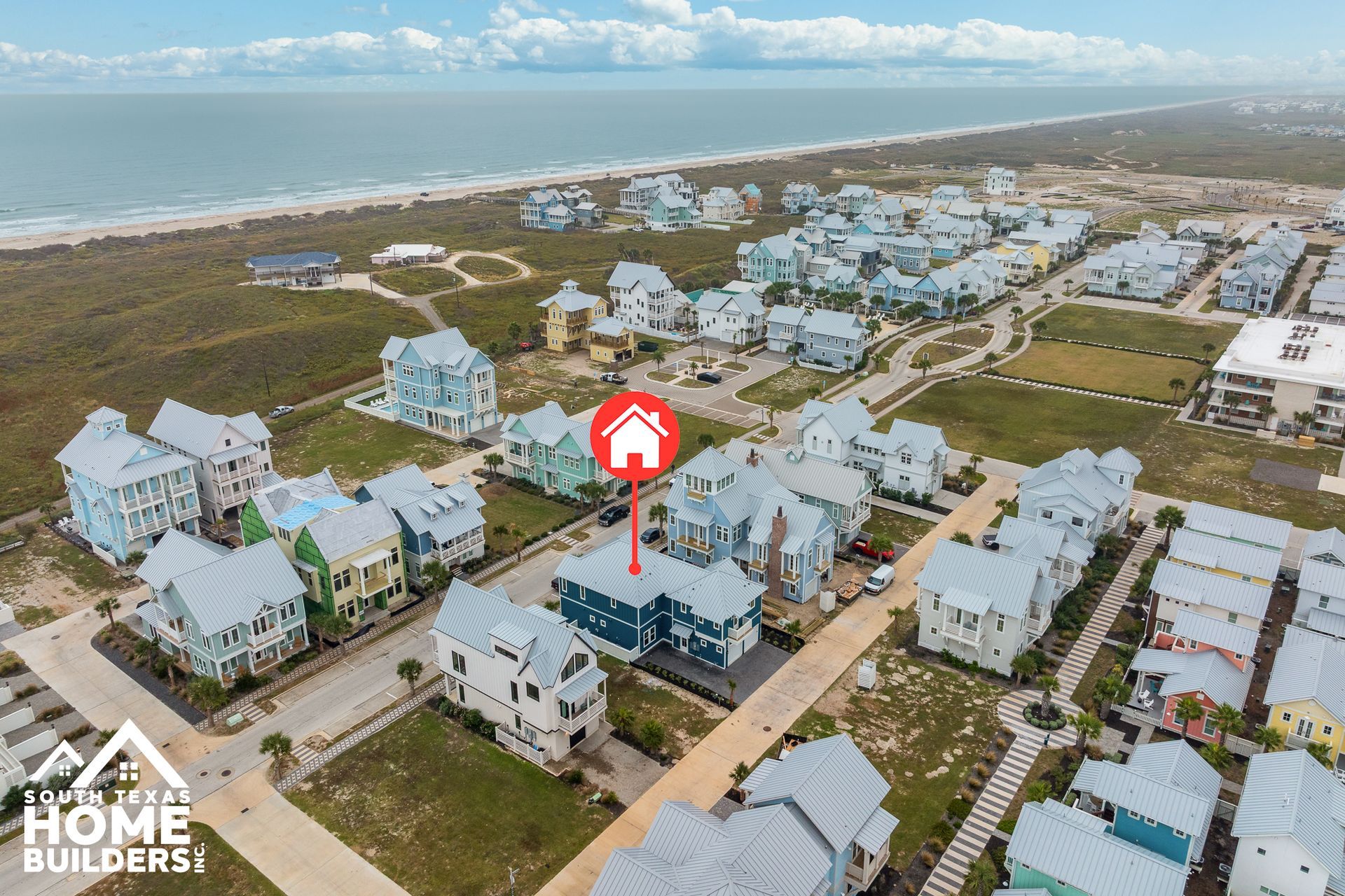 Aerial view of colorful beach houses near the ocean with a red house icon marker.