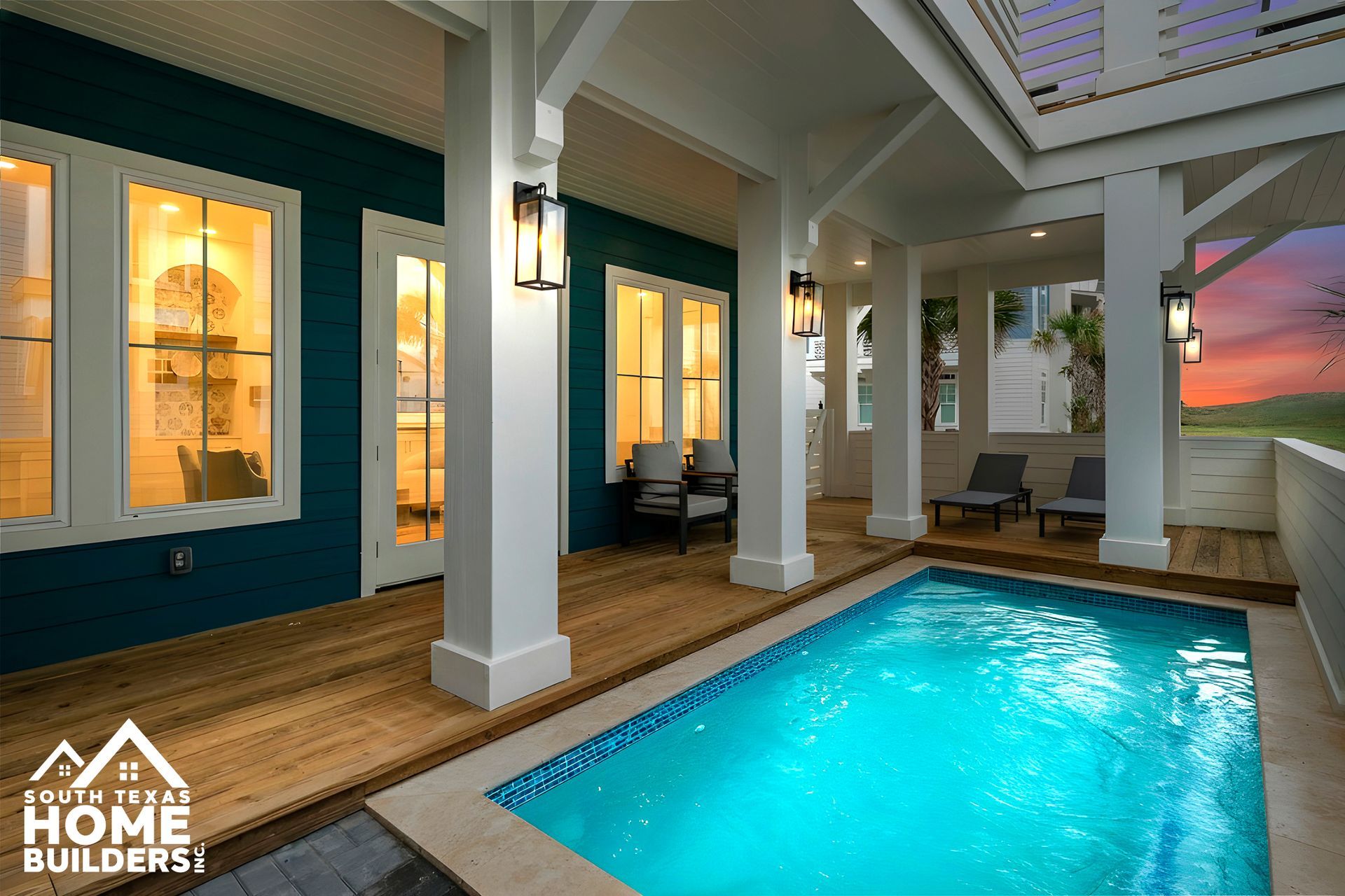 Pool area with blue water, wooden deck, white columns, and teal siding.