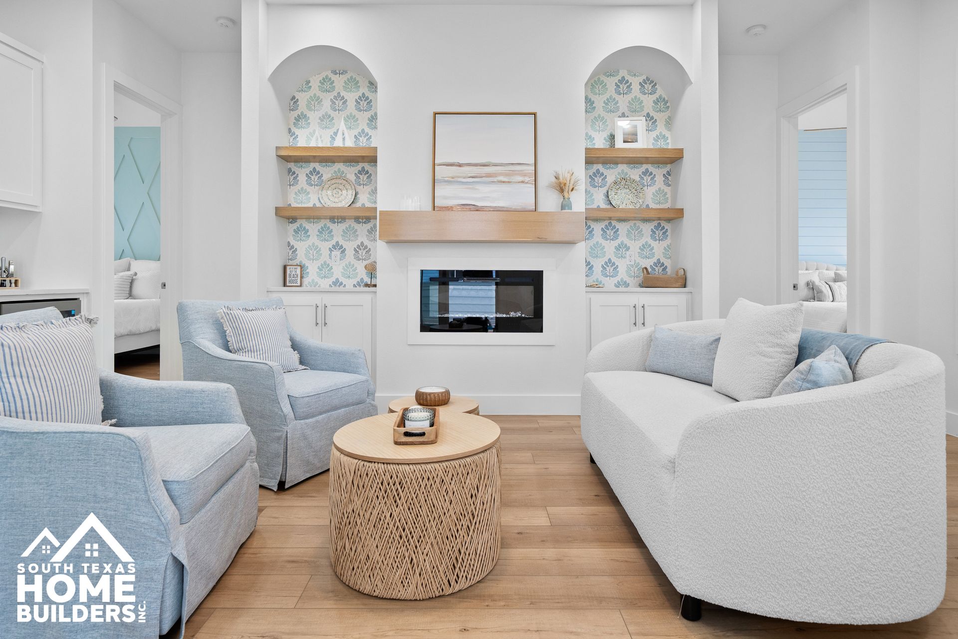 Living room with light blue armchairs, white sofa, woven coffee table, and built-in fireplace.