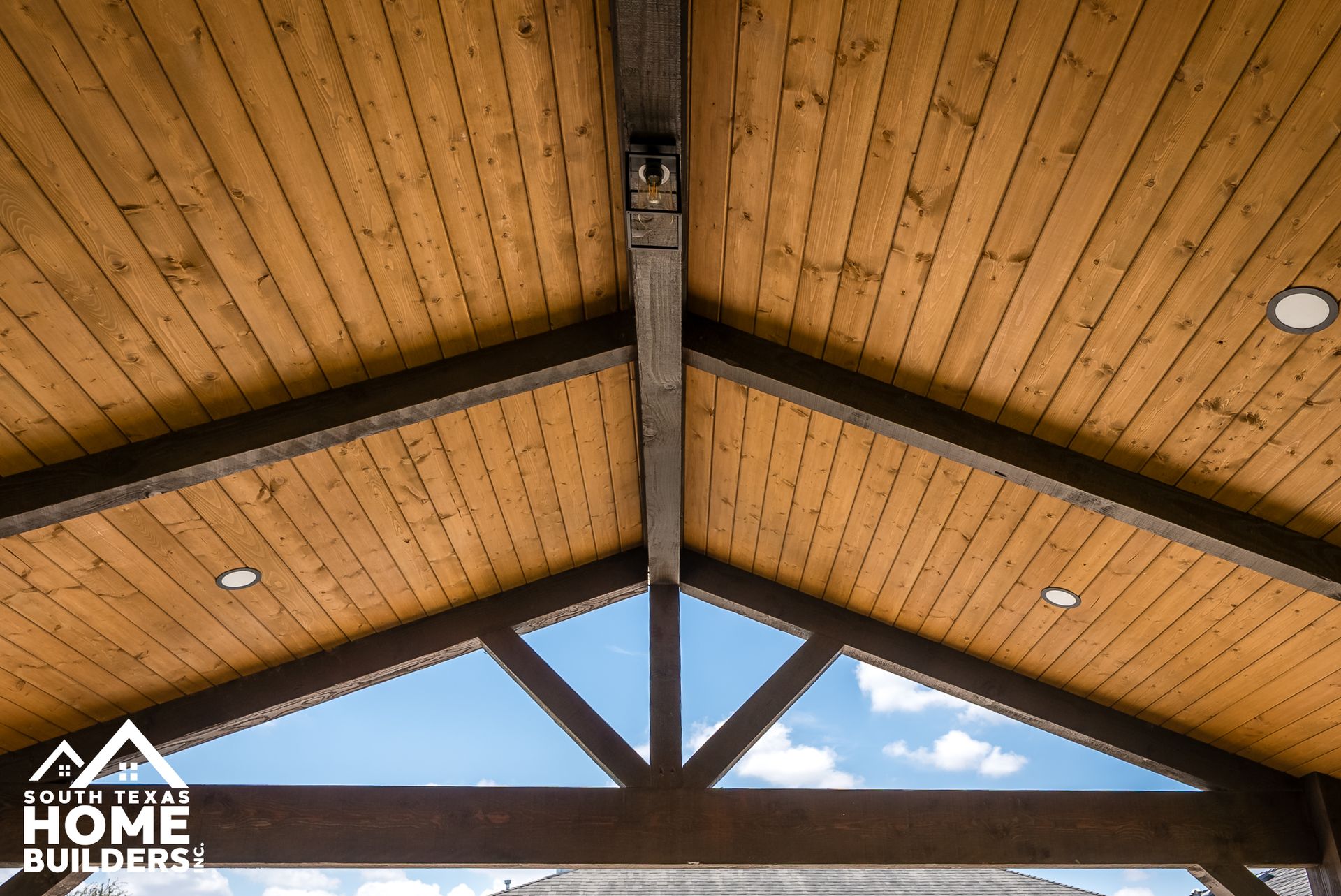 Wooden ceiling with exposed beams, recessed lights, and a view of the sky.