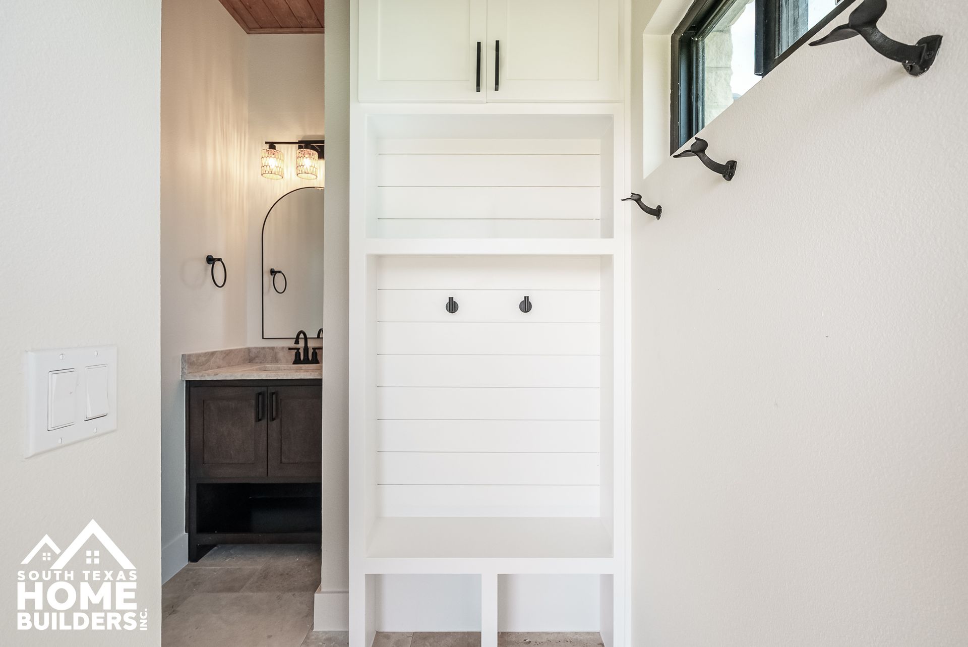 White built-in storage unit with hooks, in an entryway. Adjacent is a bathroom with a vanity.