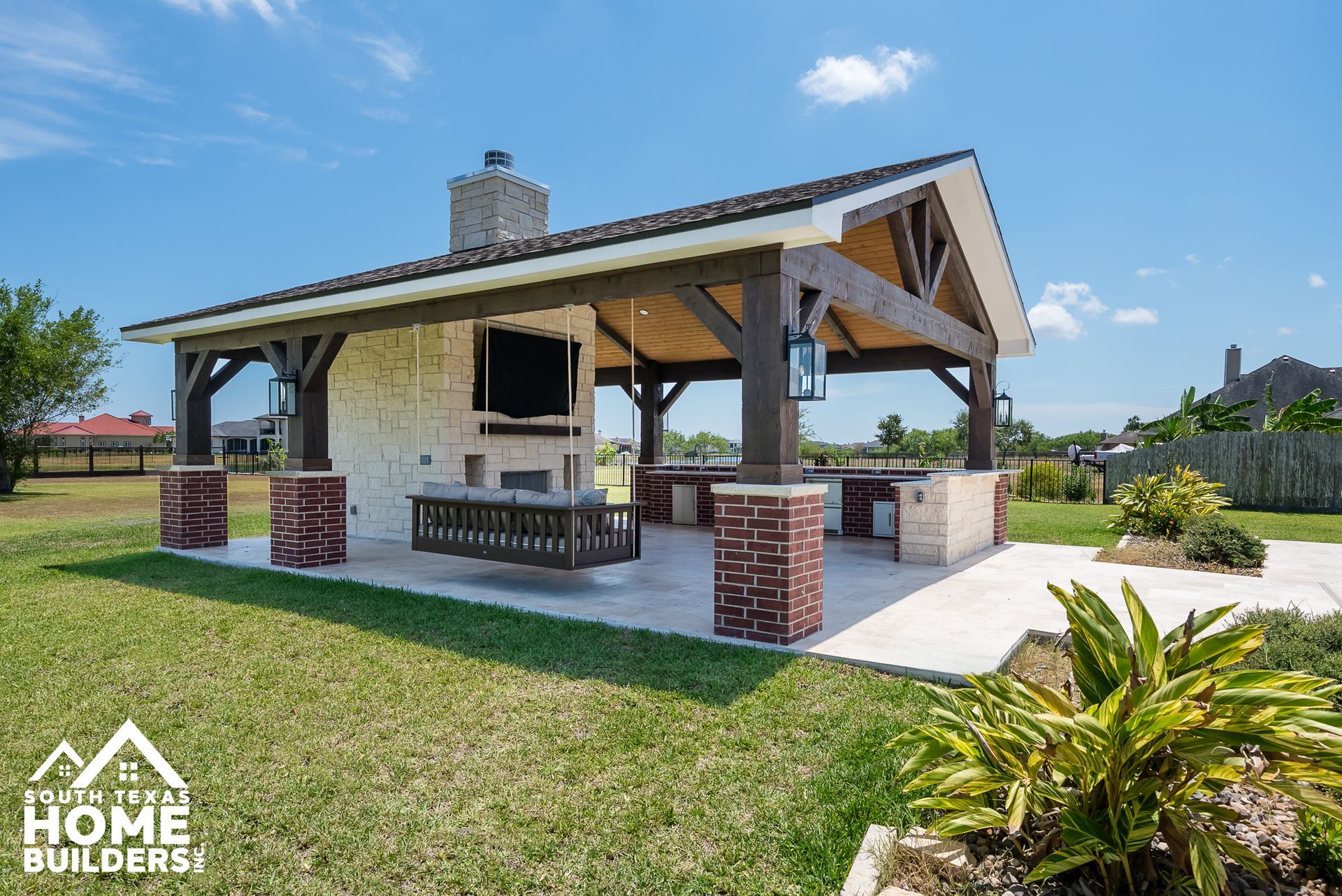 Outdoor kitchen with fireplace, TV, and seating under a covered pavilion.
